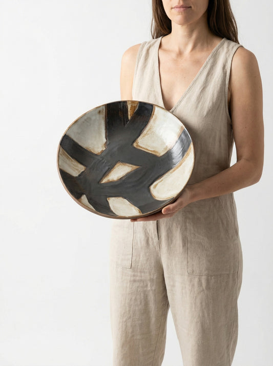 Person holding a ceramic art bowl with abstract design on a plain background