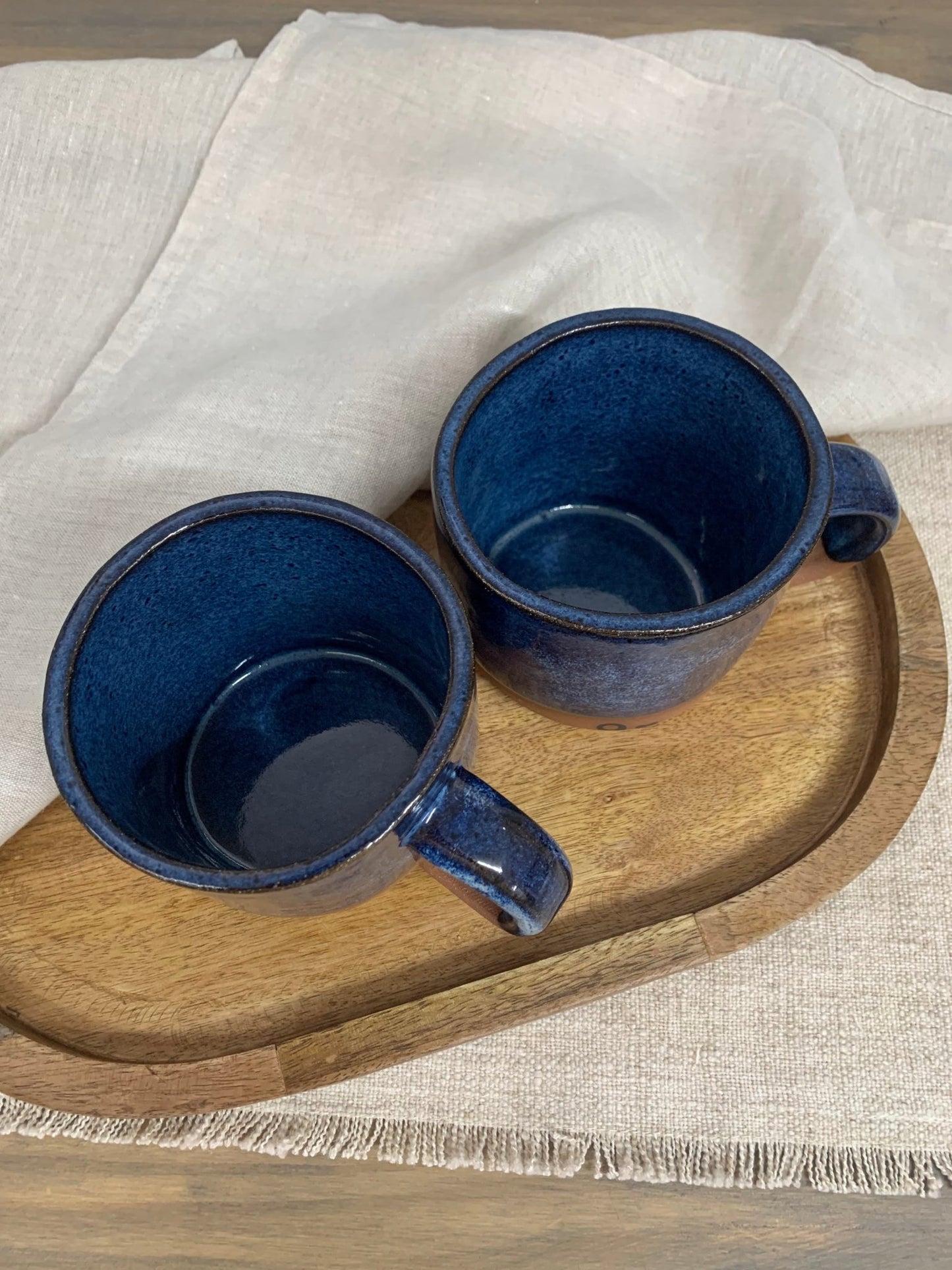 Two blue ceramic mugs on a wooden tray with a neutral background