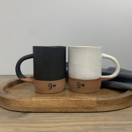 Two handmade ceramic mugs with numbers on a wooden tray against a gray background