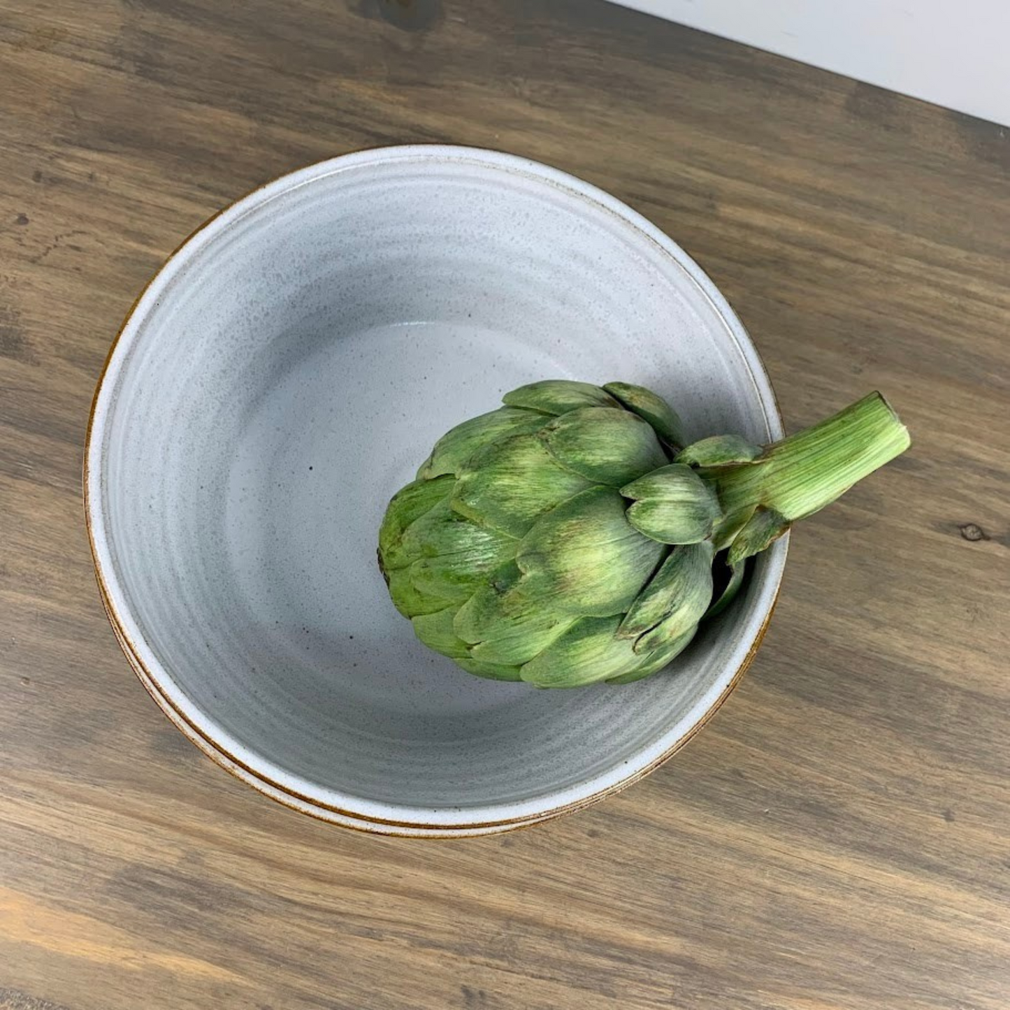 Artichoke in a white ceramic bowl on a wooden surface
