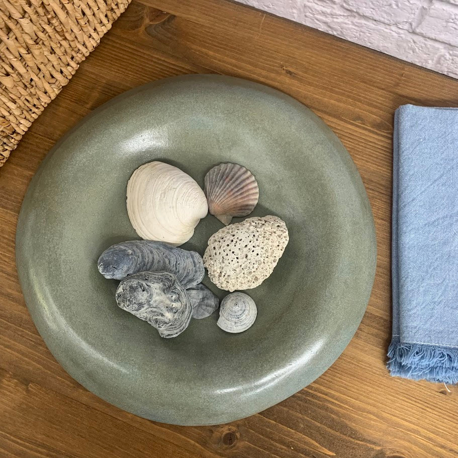 Green ceramic bowl with seashells on a wooden surface