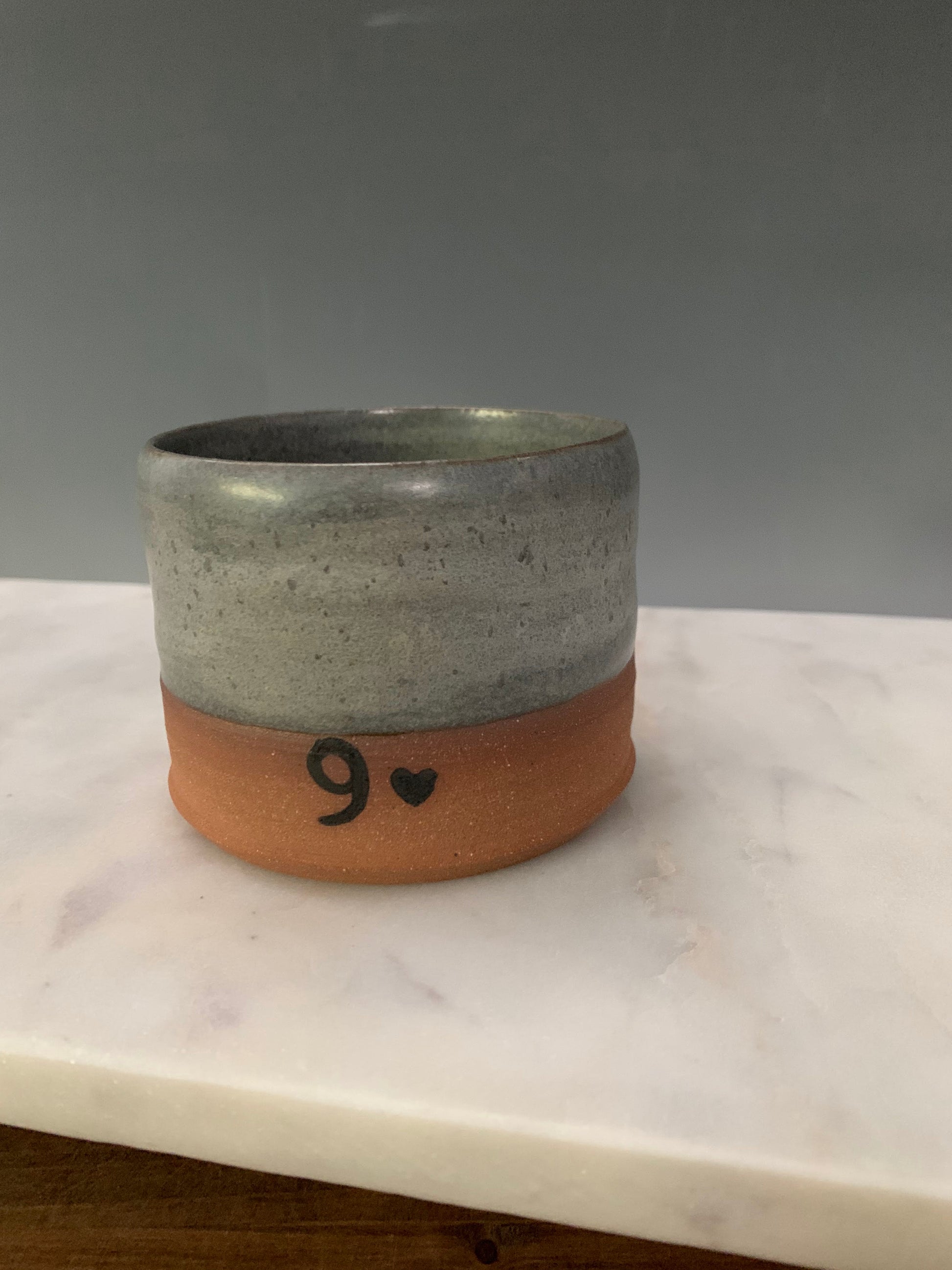 pottery cup with gray glaze and a 9 and a heart image near the bottom