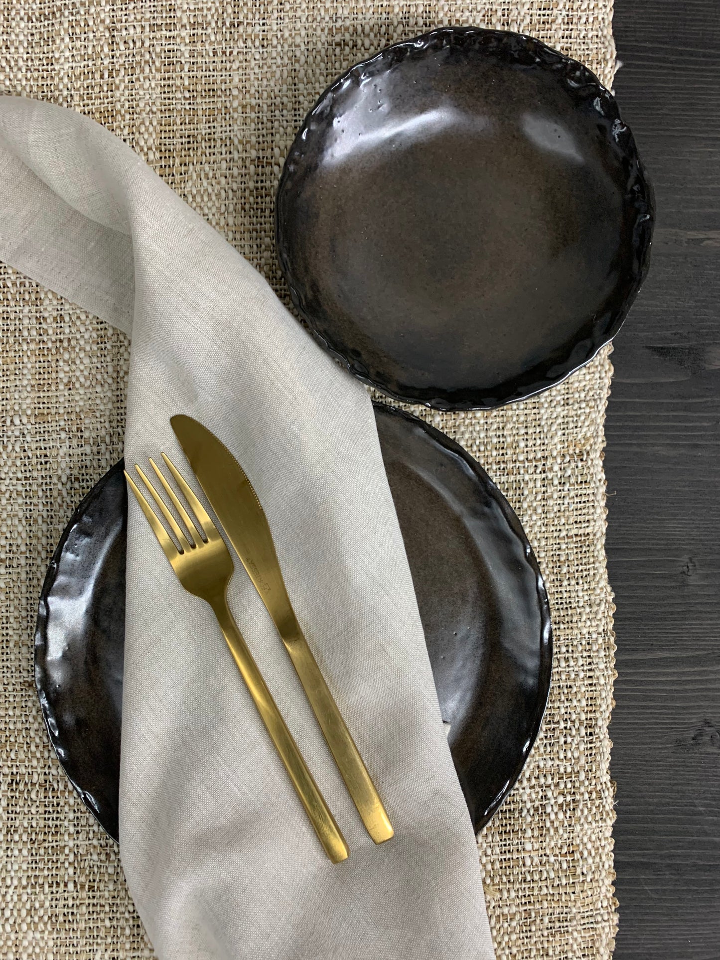 Black ceramic plates with gold cutlery on a textured surface