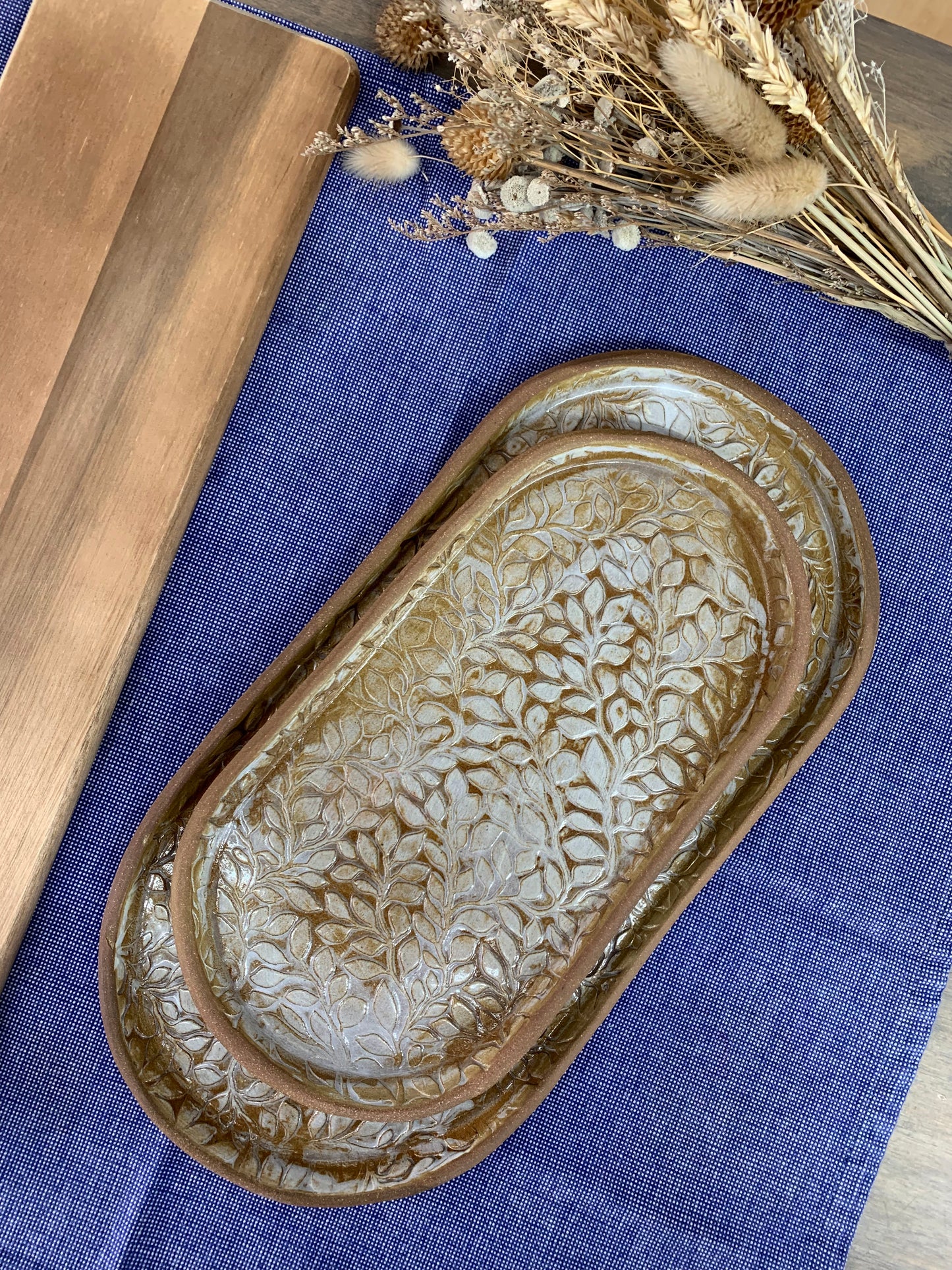 Decorative artisan ceramic tray set with intricate leaf patterns on a blue fabric background
