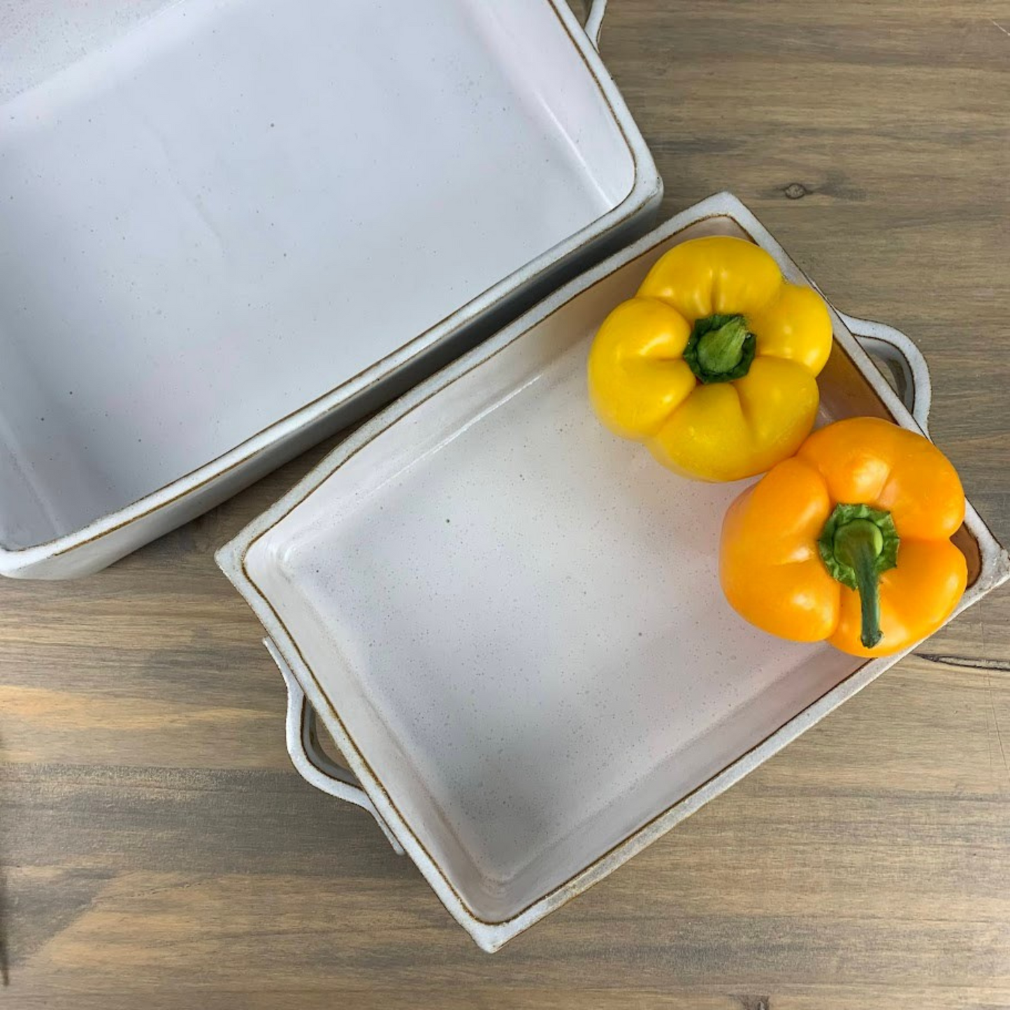 Two rectangular ceramic casserole dishes. One has two bell peppers inside. One is yellow, one orange.