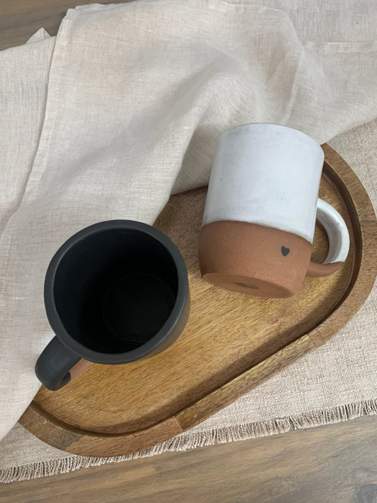 Two ceramic mugs, one black and one white with a brown base, on a wooden tray.