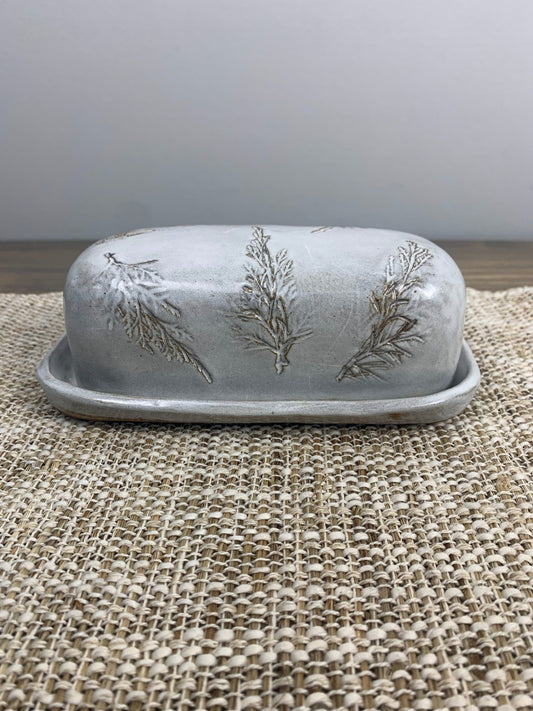 Decorative butter dish with fresh pine patterns on a textured surface
