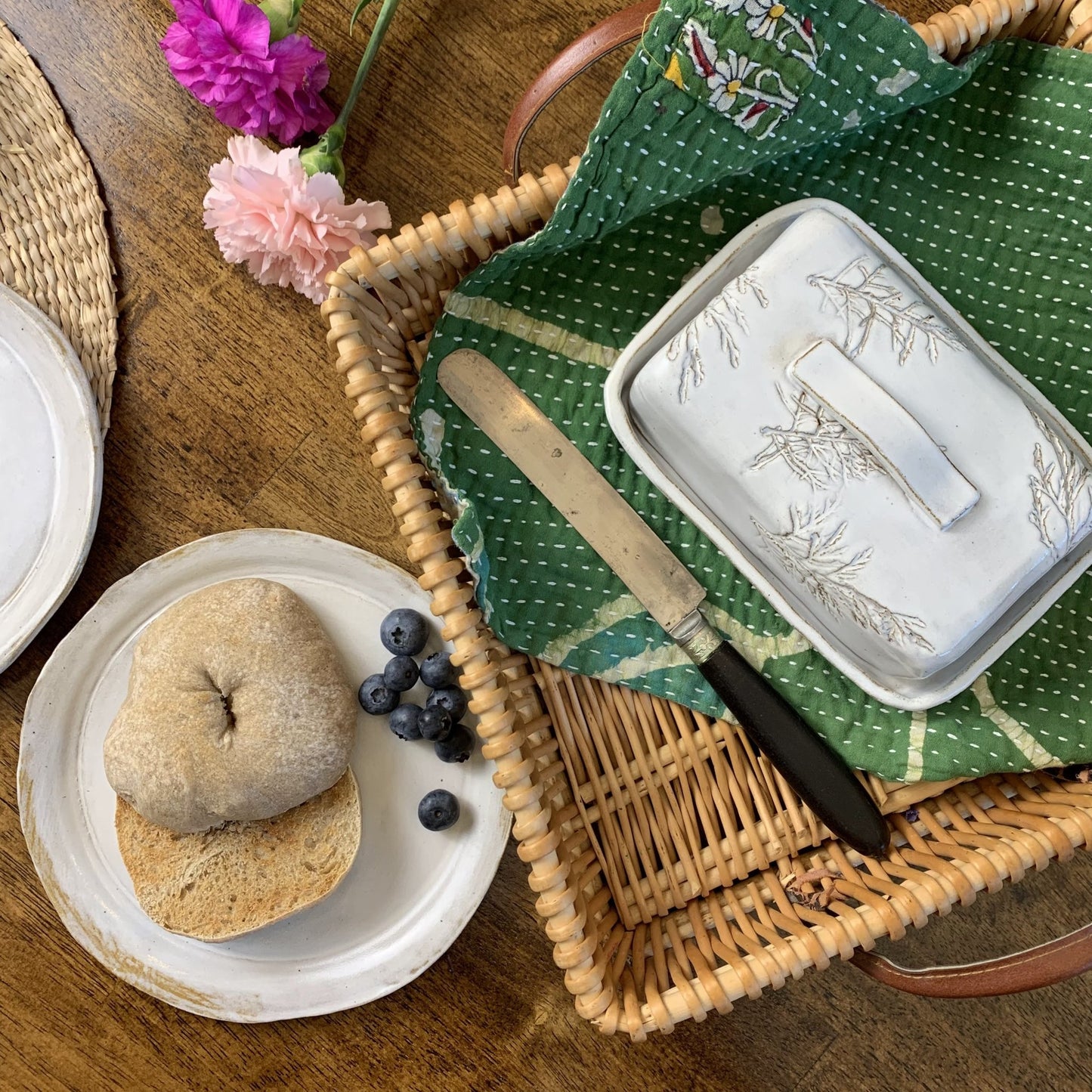 White handmade ceramic butter dish on wooden surface next to a bagel