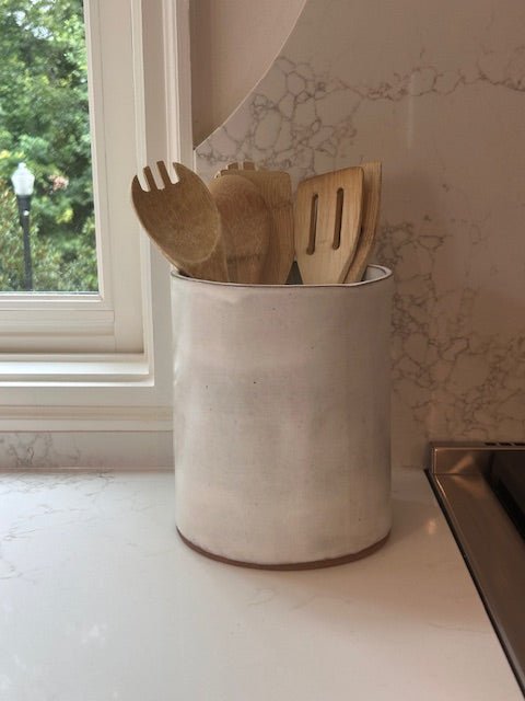 Handmade ceramic utensil holder with wooden utensils on a kitchen counter.