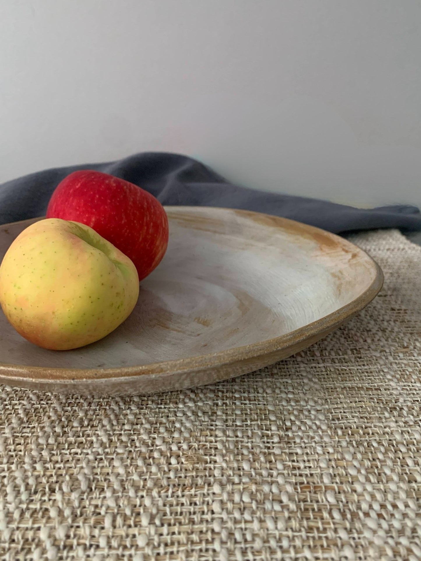 Two apples on a handmade ceramic plate with a gray napkin and textured surface
