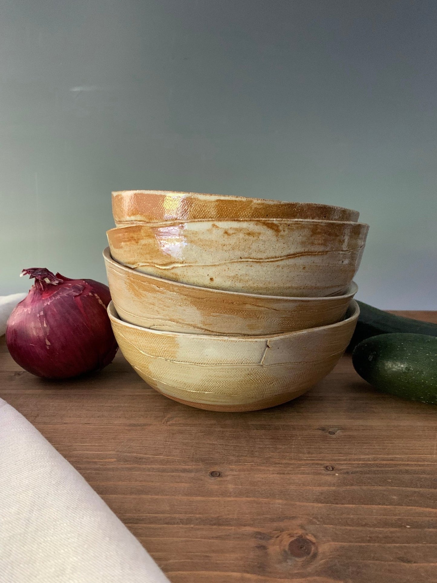 Stack of ceramic bowls on a wooden surface with a red onion and green zucchini.