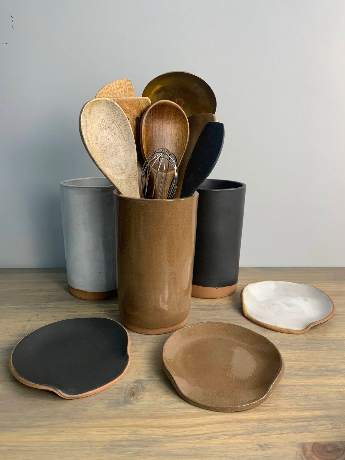 Set of ceramic utensil holders and spoon rests on a wooden surface with a neutral background