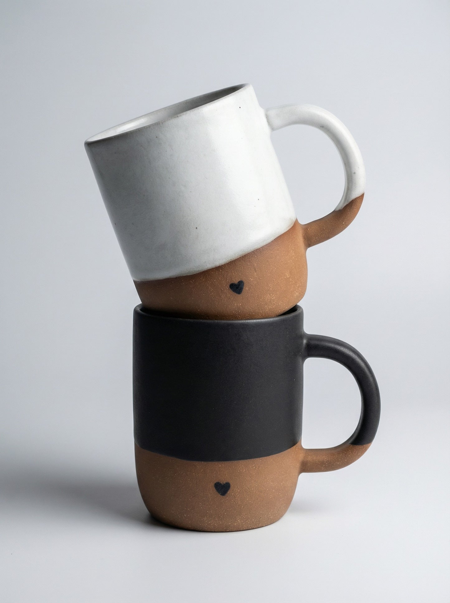 Two handmade pottery mugs stacked on a light gray background