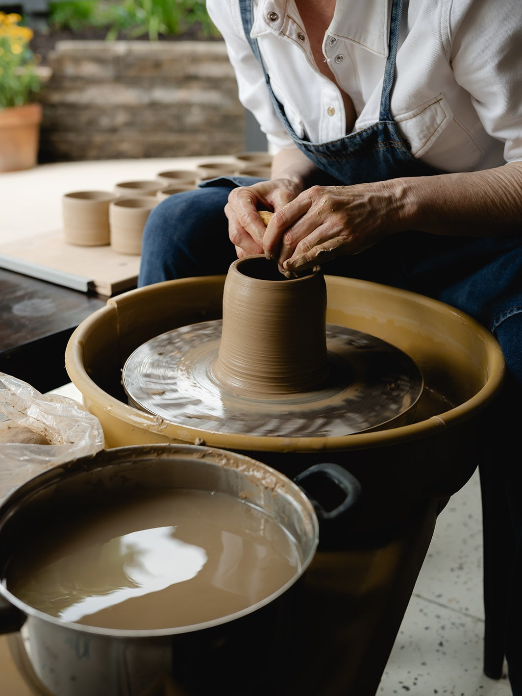 Person working with clay on a pottery wheel in a studio setting.