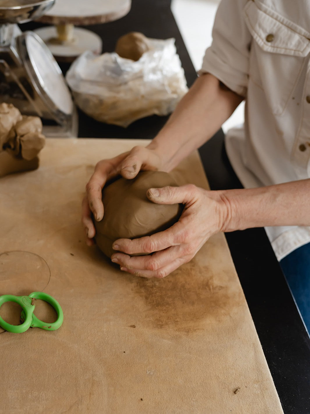Person shaping a clay object on a wooden table with a blurred background