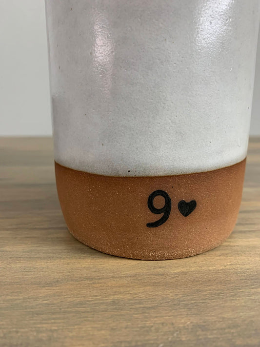 pottery vase closeup with a brown base and number 9 on a wooden surface