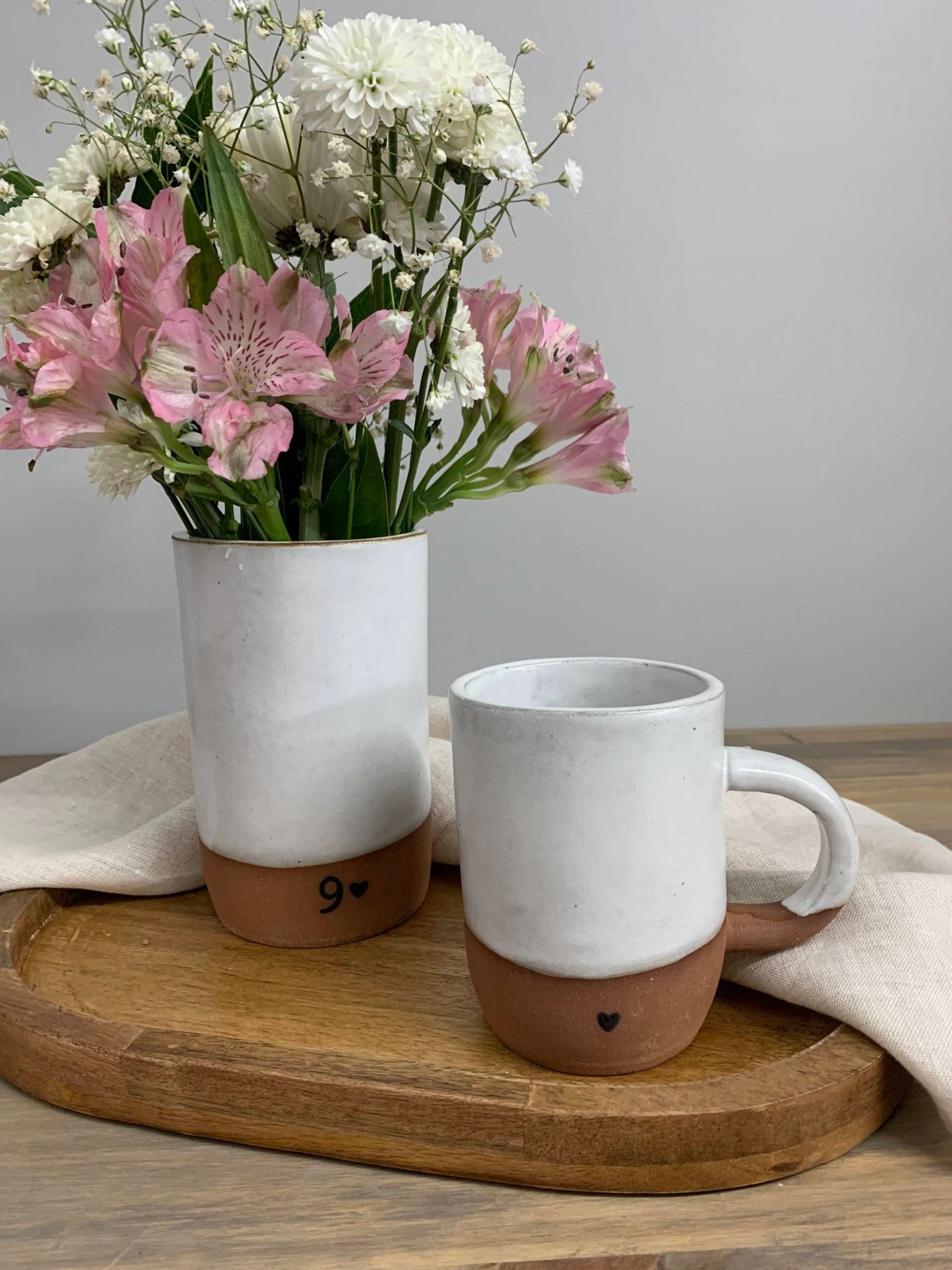 handmade pottery mug and vase with flowers on a wooden tray