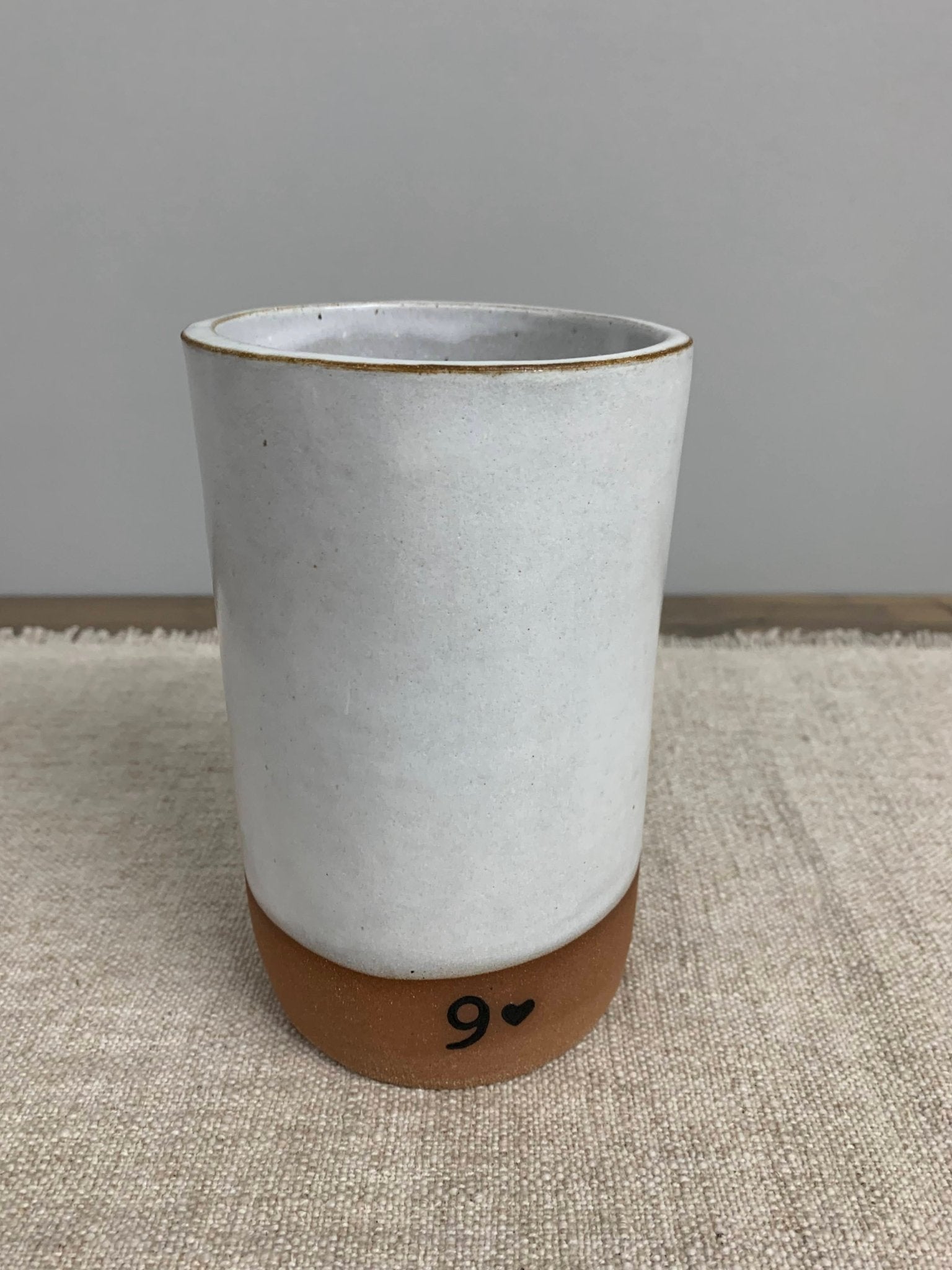 White ceramic vase with brown base and no.9 design on a textured surface