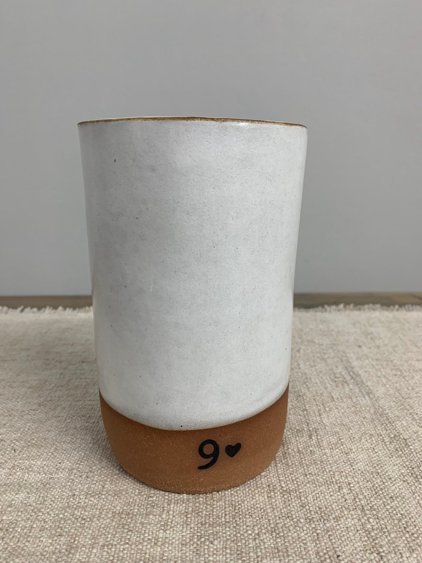Ceramic vase with a brown base and white glaze with a 9 design on a textured surface.