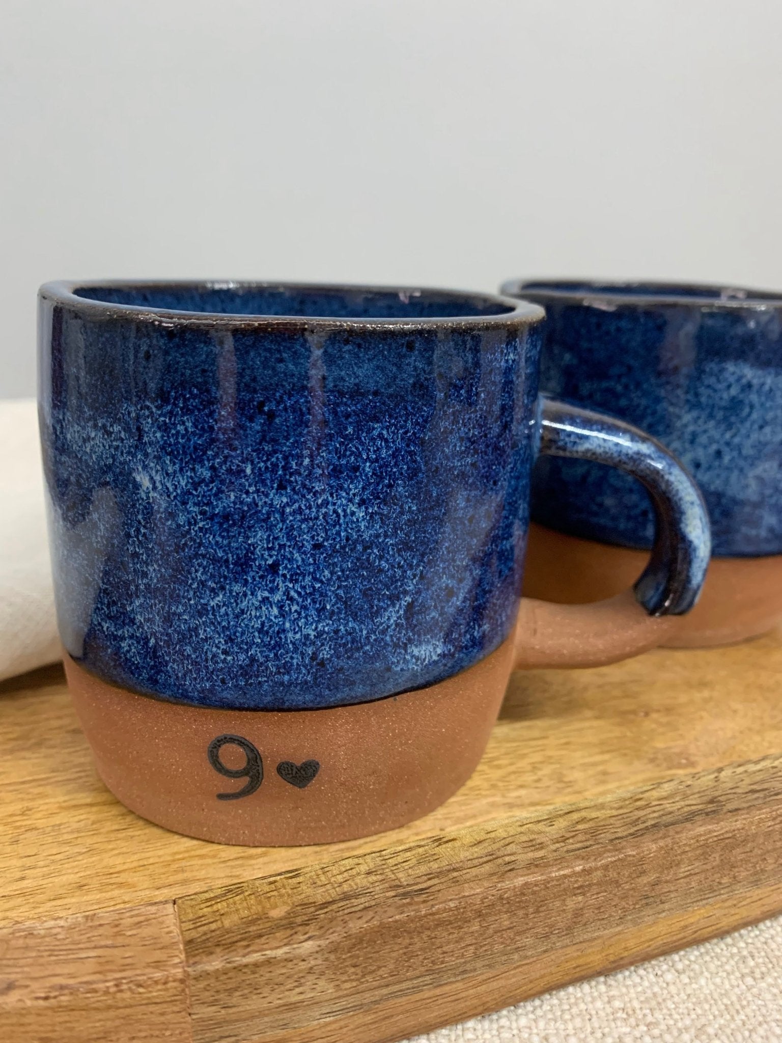 Two blue ceramic mugs with a heart and number 9 on a wooden surface.