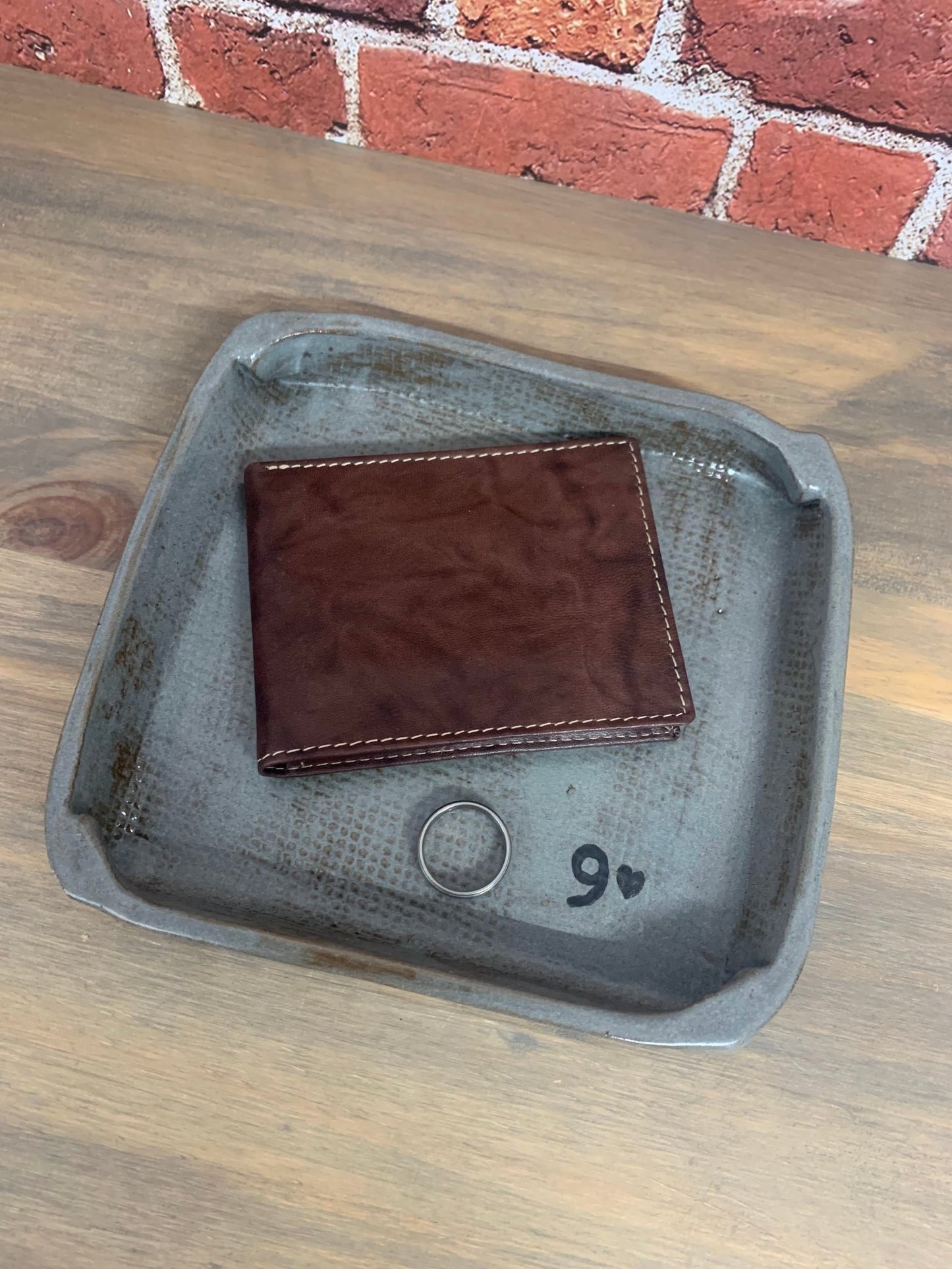 Brown leather wallet on a pottery tray stamped for 9 anniversary with a brick wall background