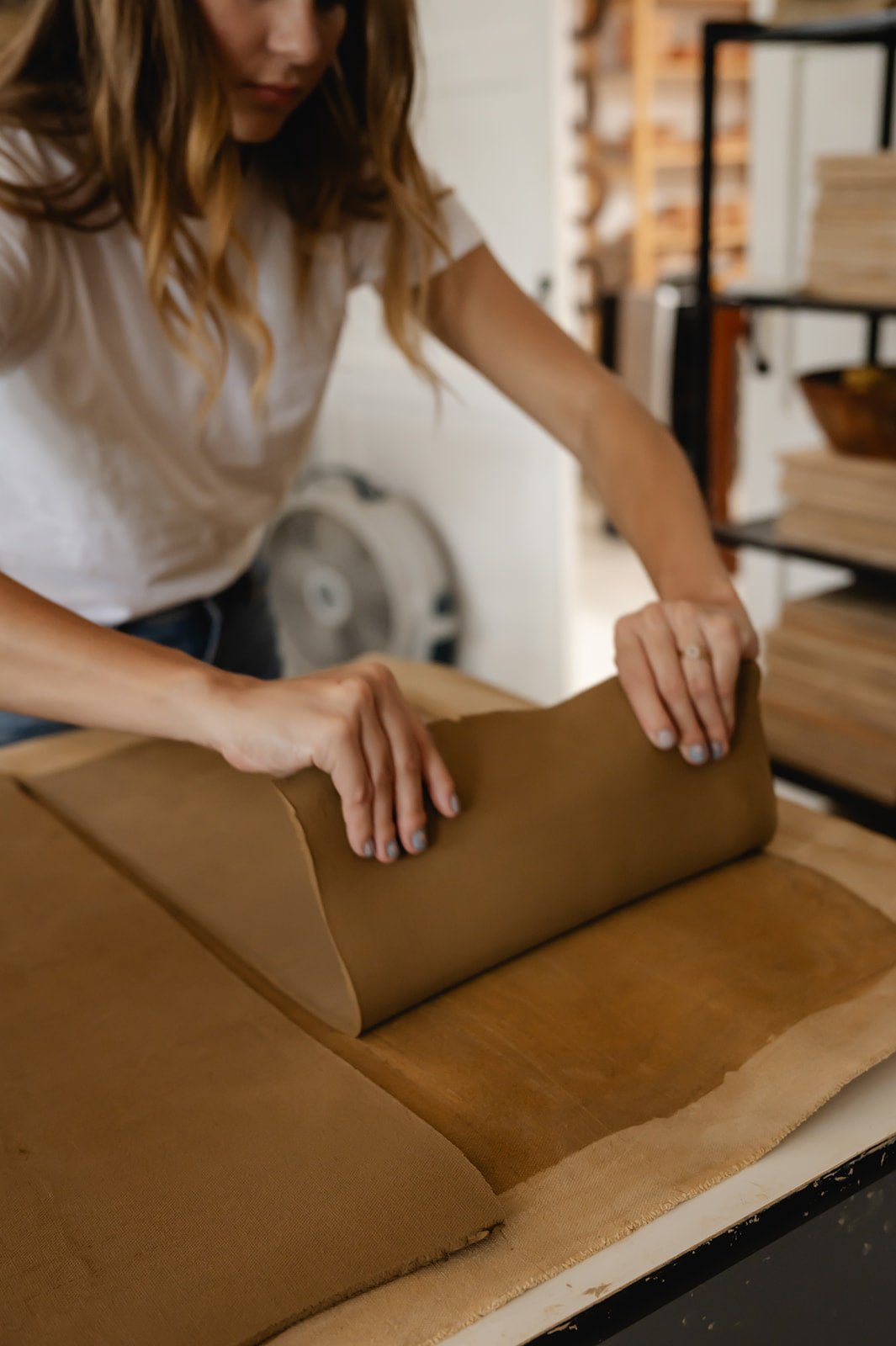 Person rolling clay on a table in a pottery studio setting