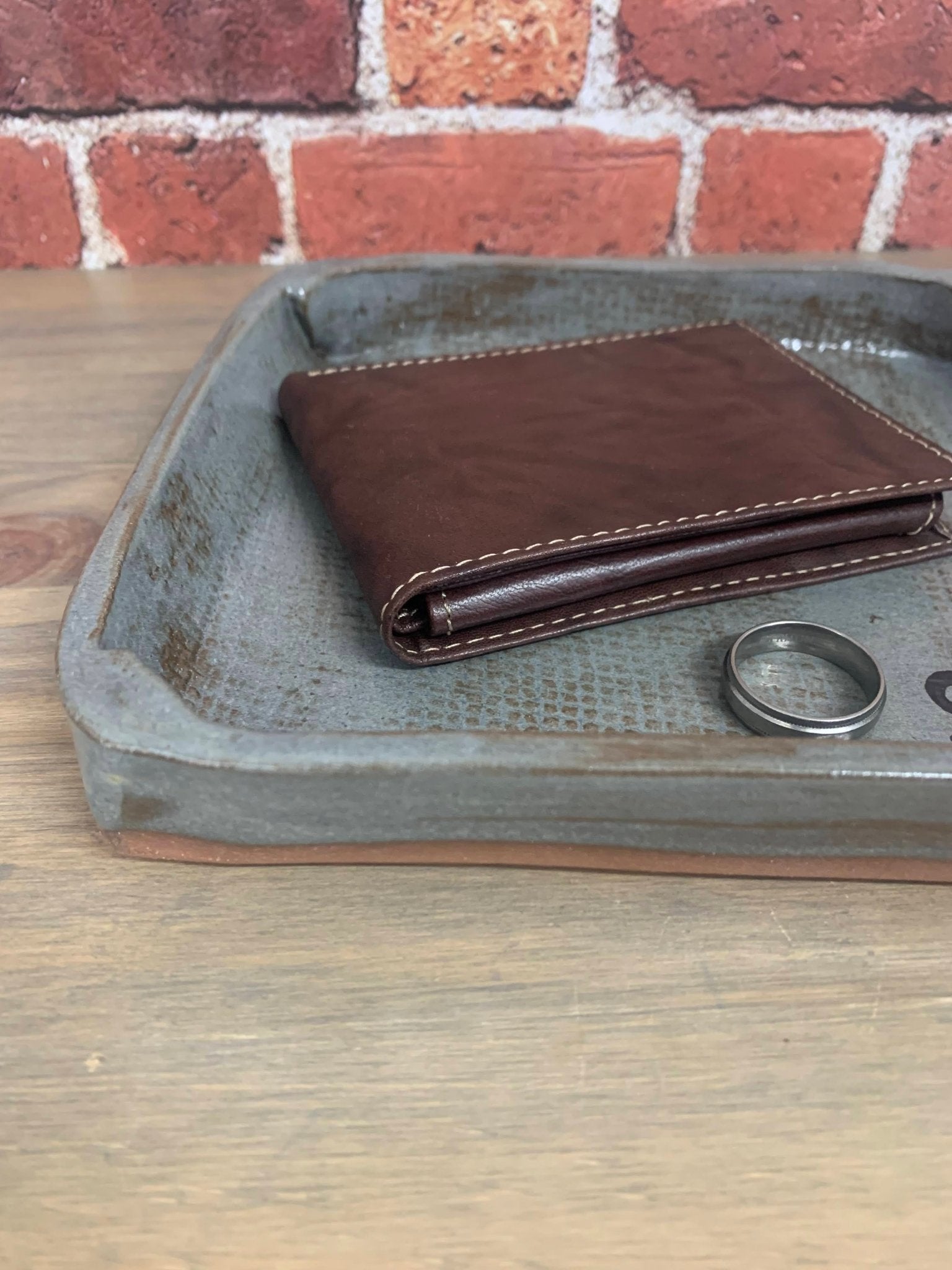 Brown leather wallet and ring on a rustic catchall anniversary tray with a brick wall background