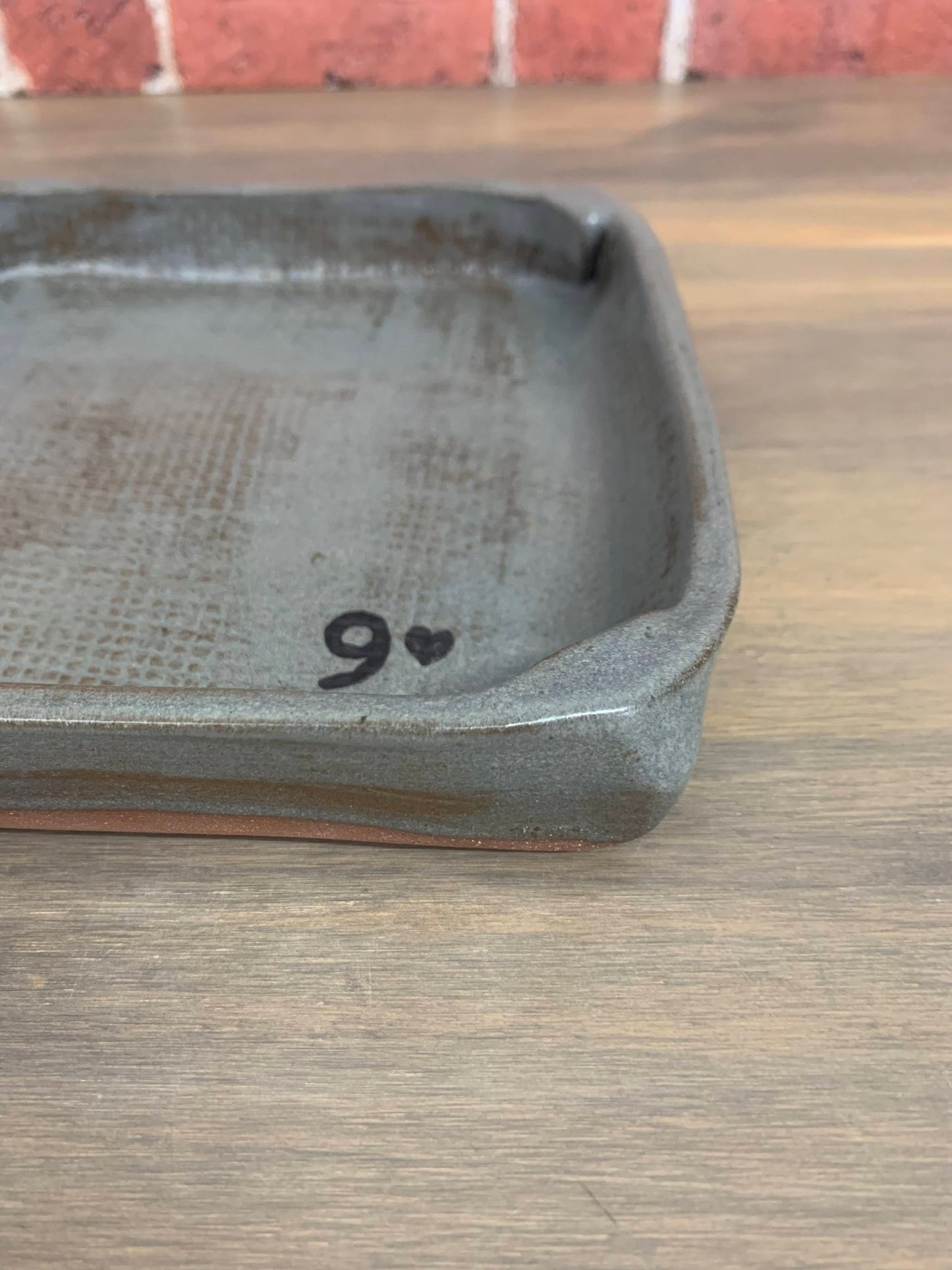 Rustic pottery catchall tray with '9' and heart symbol on a wooden surface