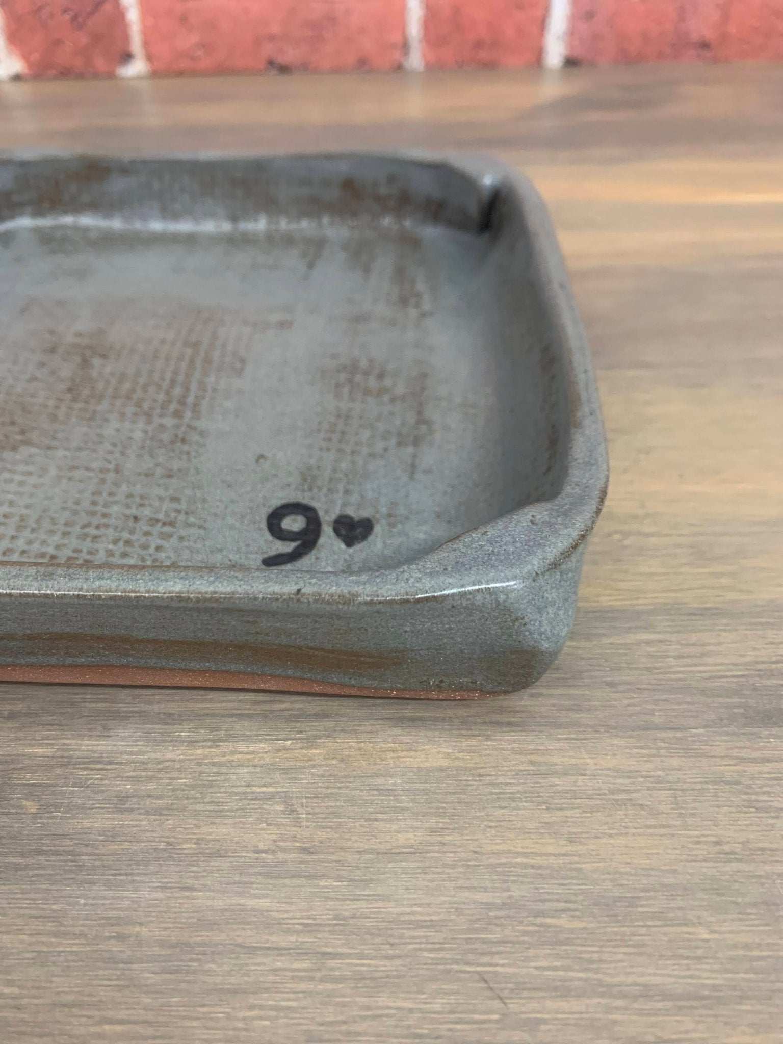 Rustic pottery catchall tray with '9' and heart symbol on a wooden surface