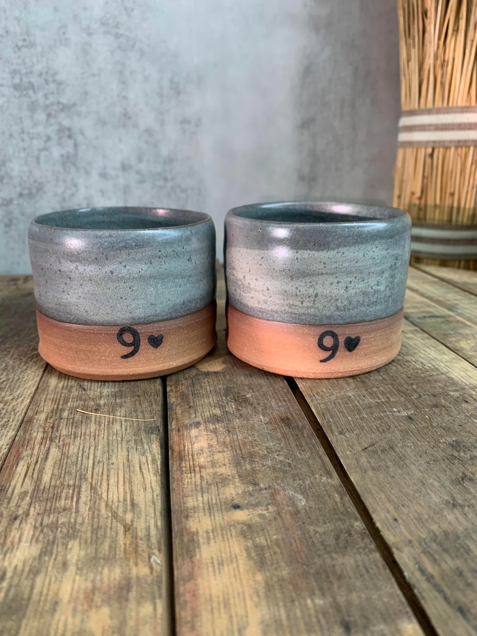 Two handmade 
ceramic cups with a number '9' and heart symbol on a wooden surface.