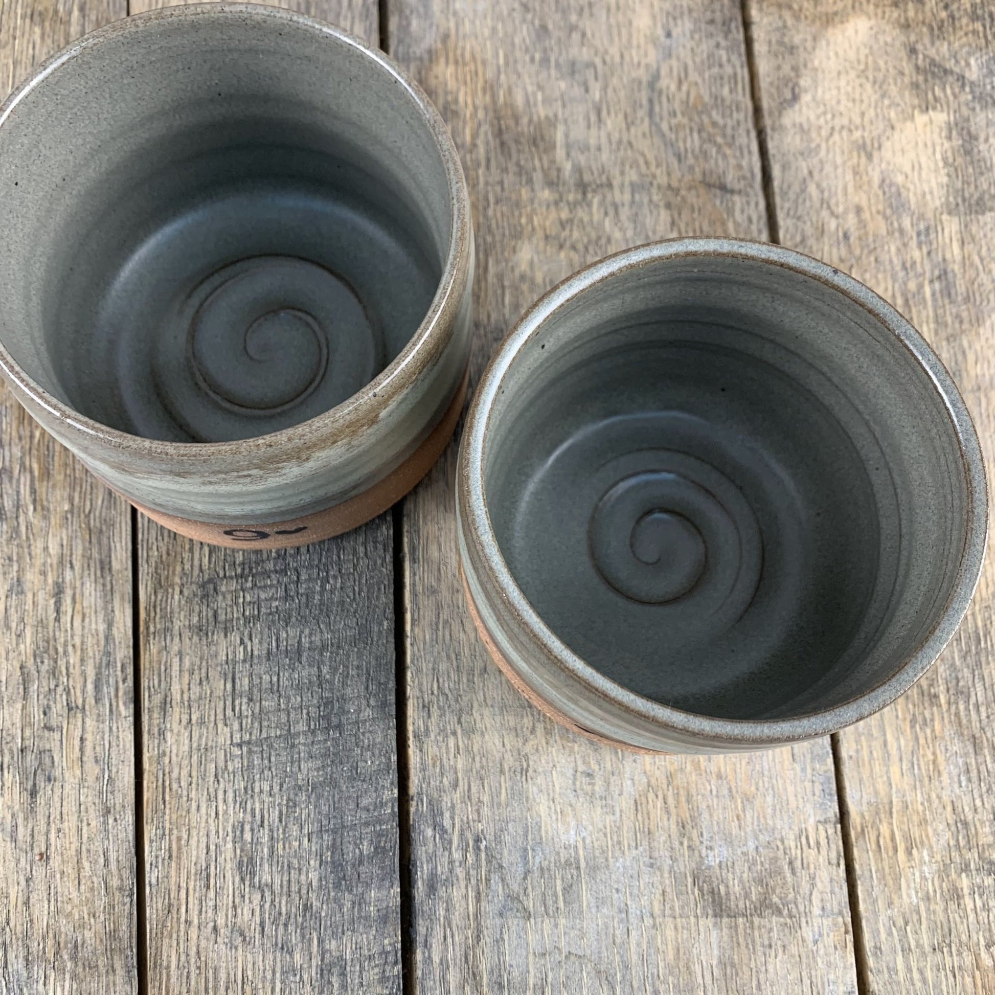 Two gray ceramic mugs with no handles, top view with spiral design on inside bottom on a wooden surface
