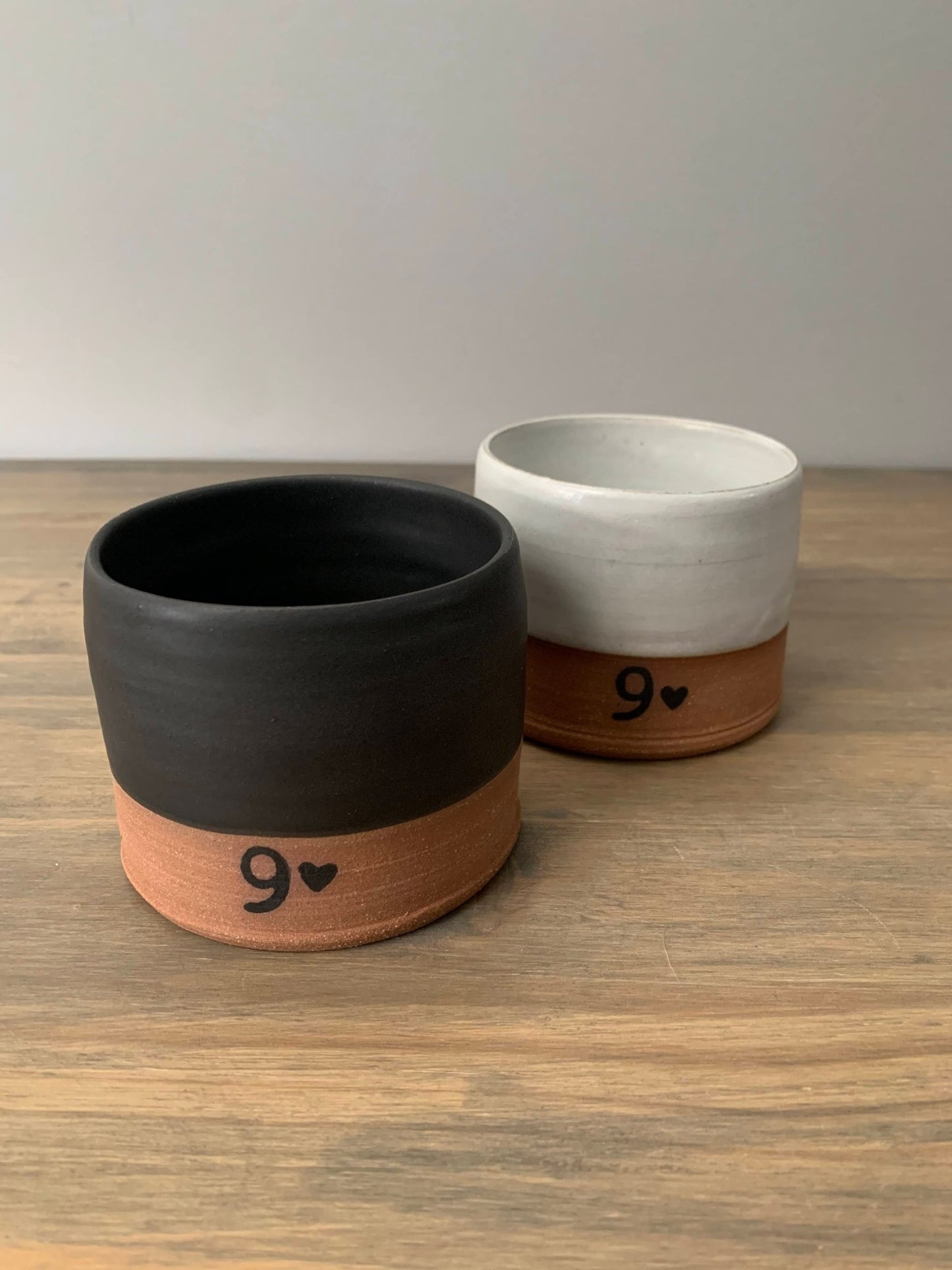 two pottery mugs with 9 design on a wooden surface