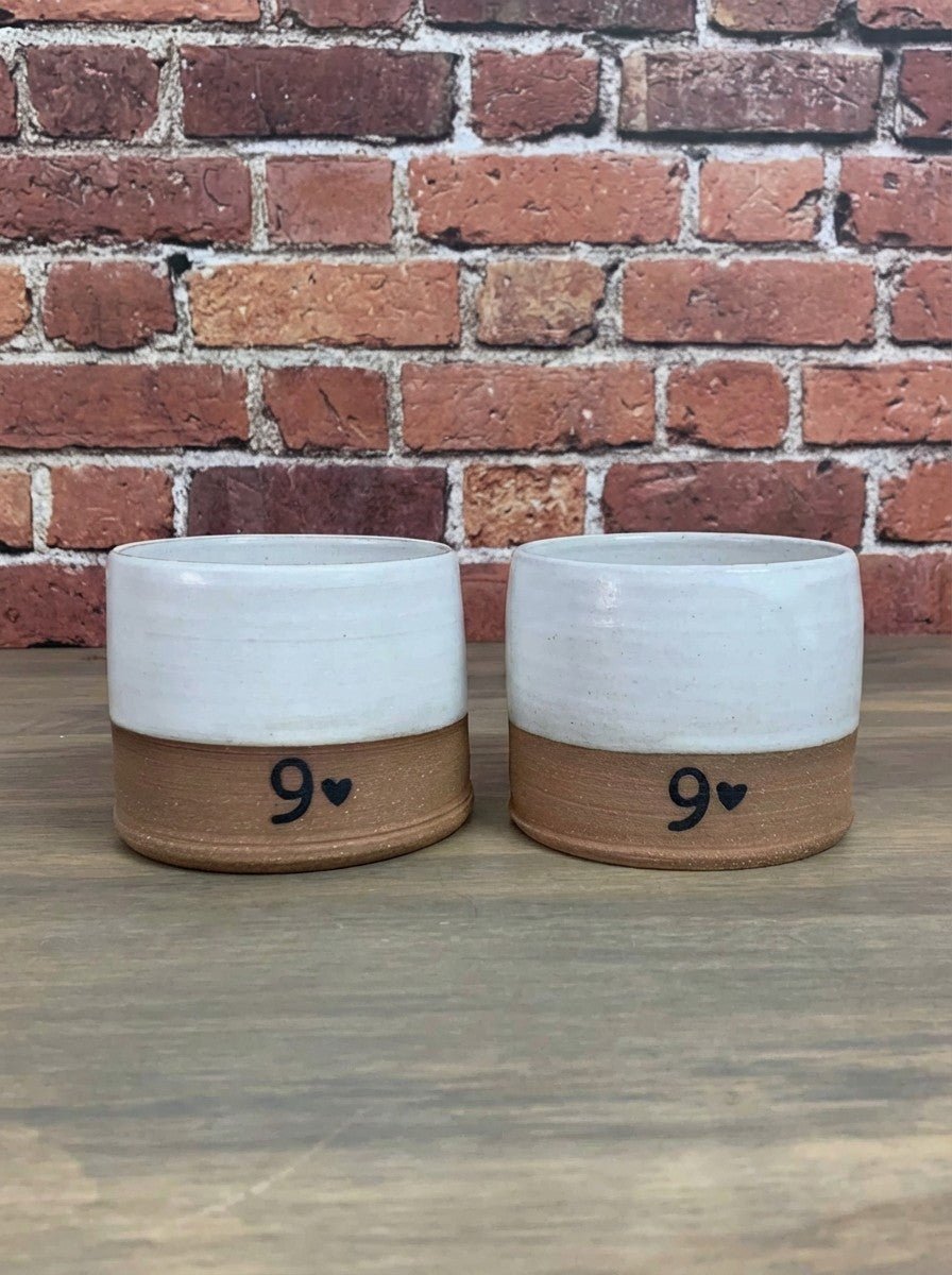 pottery glasses with a heart design on a wooden surface against a brick wall.