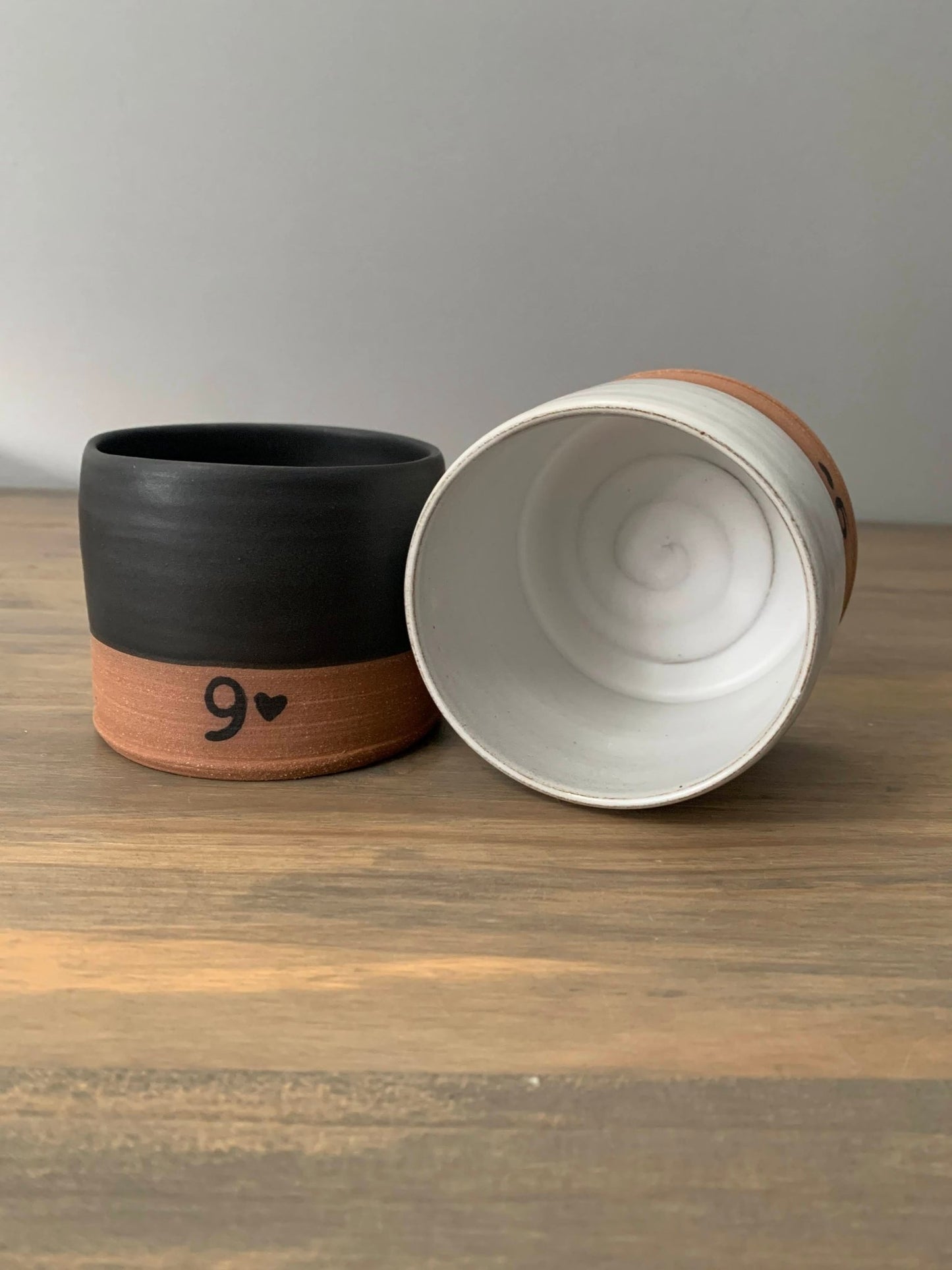 Two ceramic pottery mugs with no handles on a wooden surface