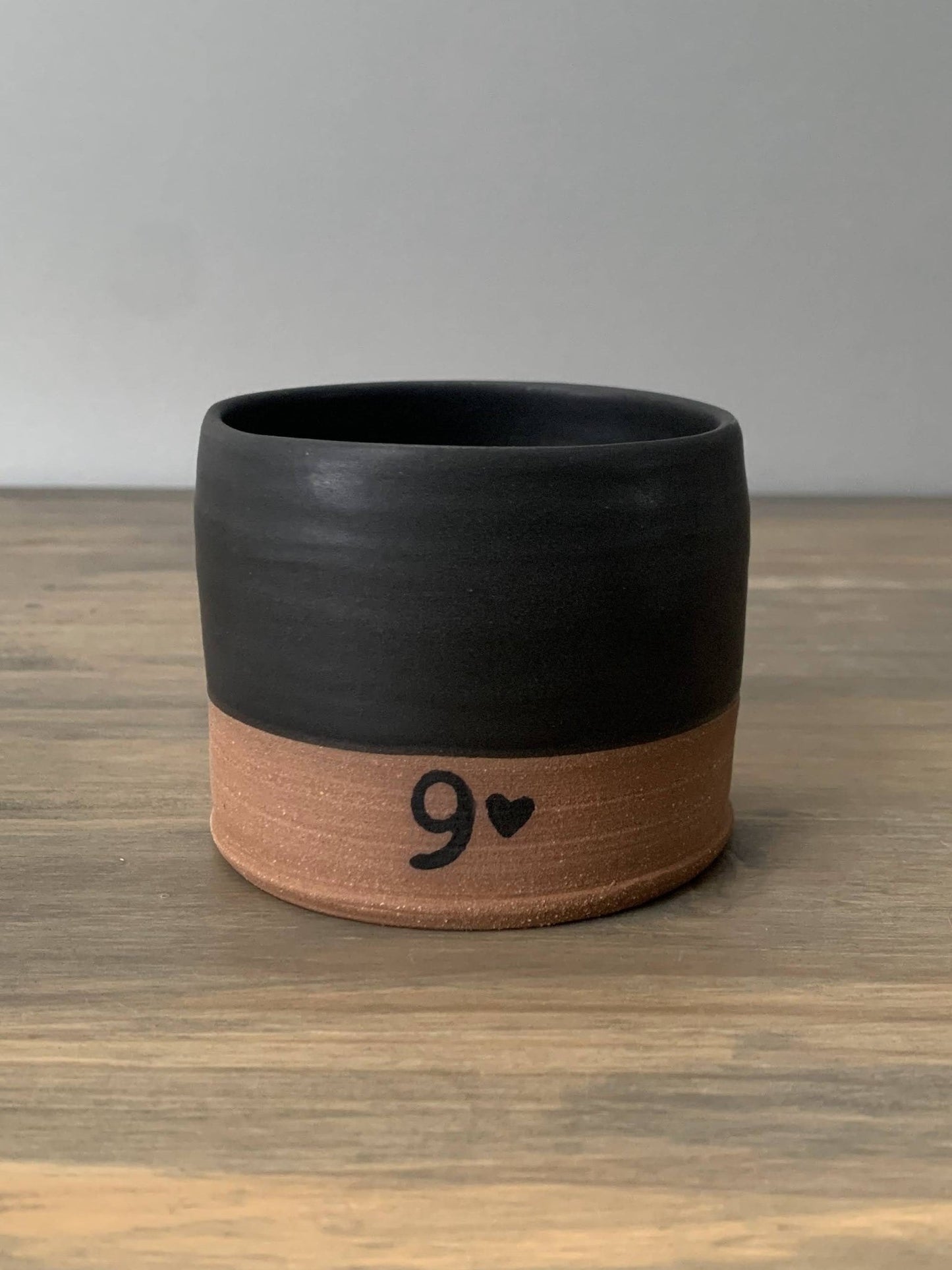 Black and brown pottery cup with number 9 and heart on a wooden surface