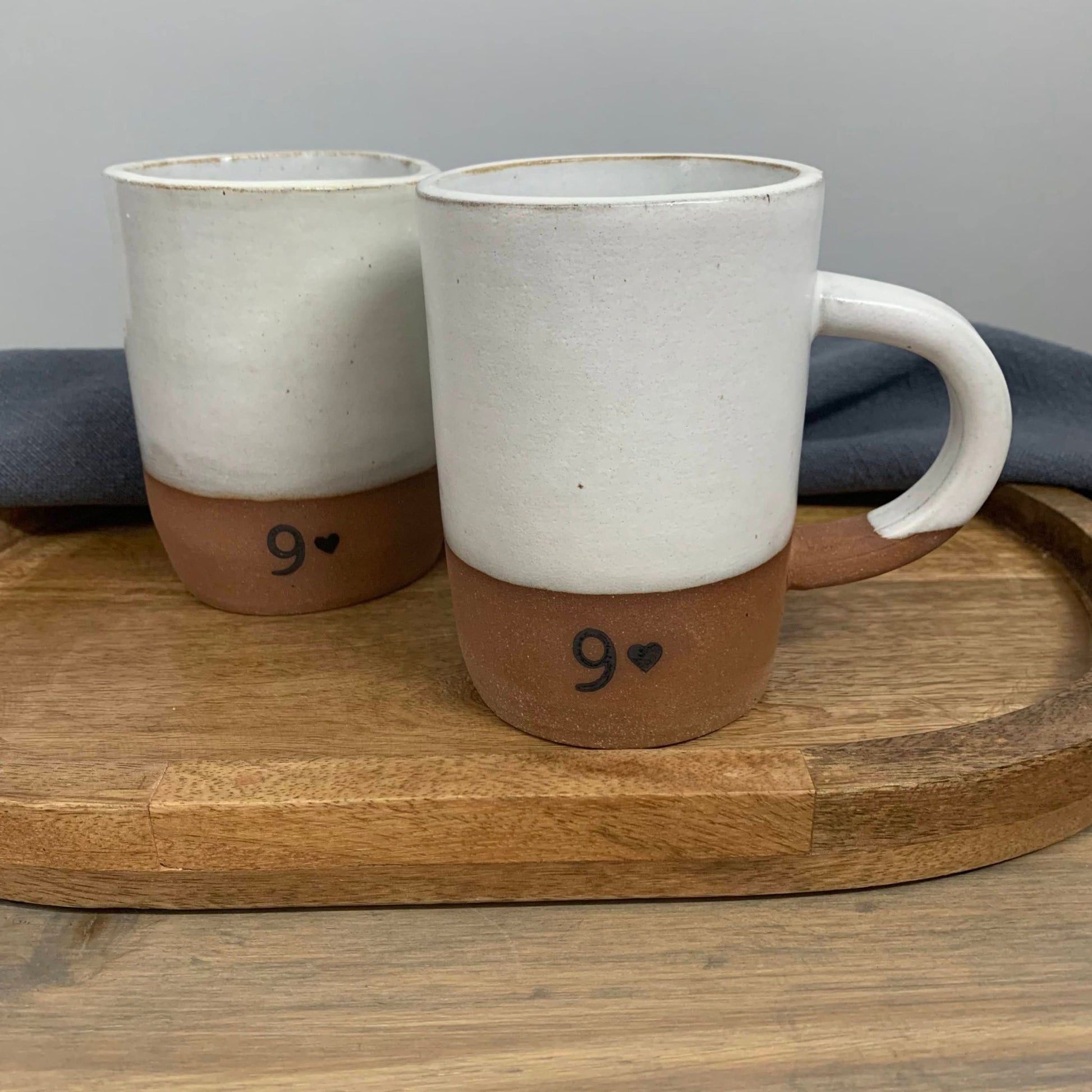 Two pottery mugs with 9 design on a wooden tray