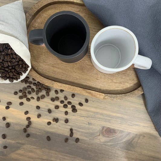 Two handmade ceramic mugs on a wooden tray with coffee beans