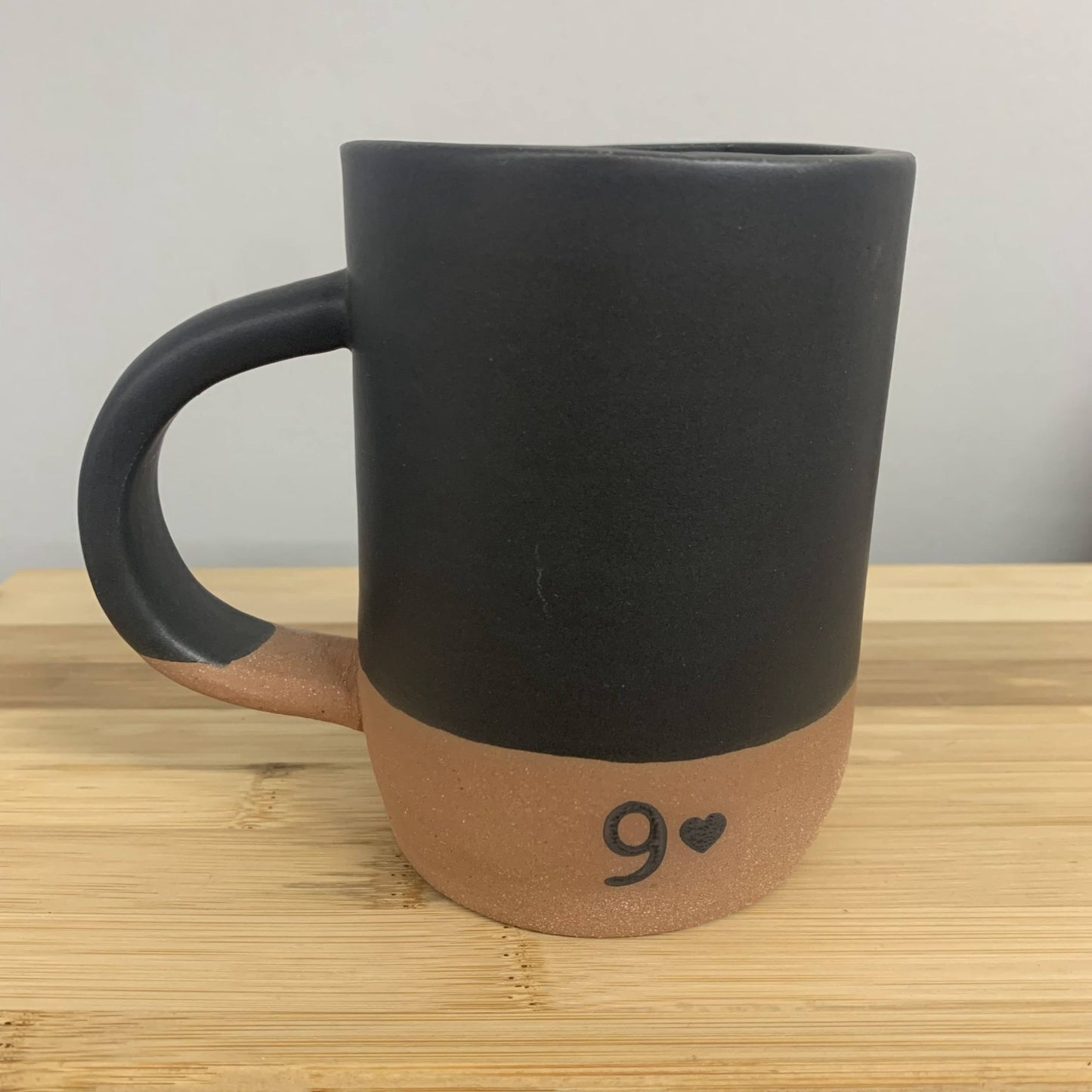 Black handmade mug with a brown base and number 9 heart design on a wooden surface