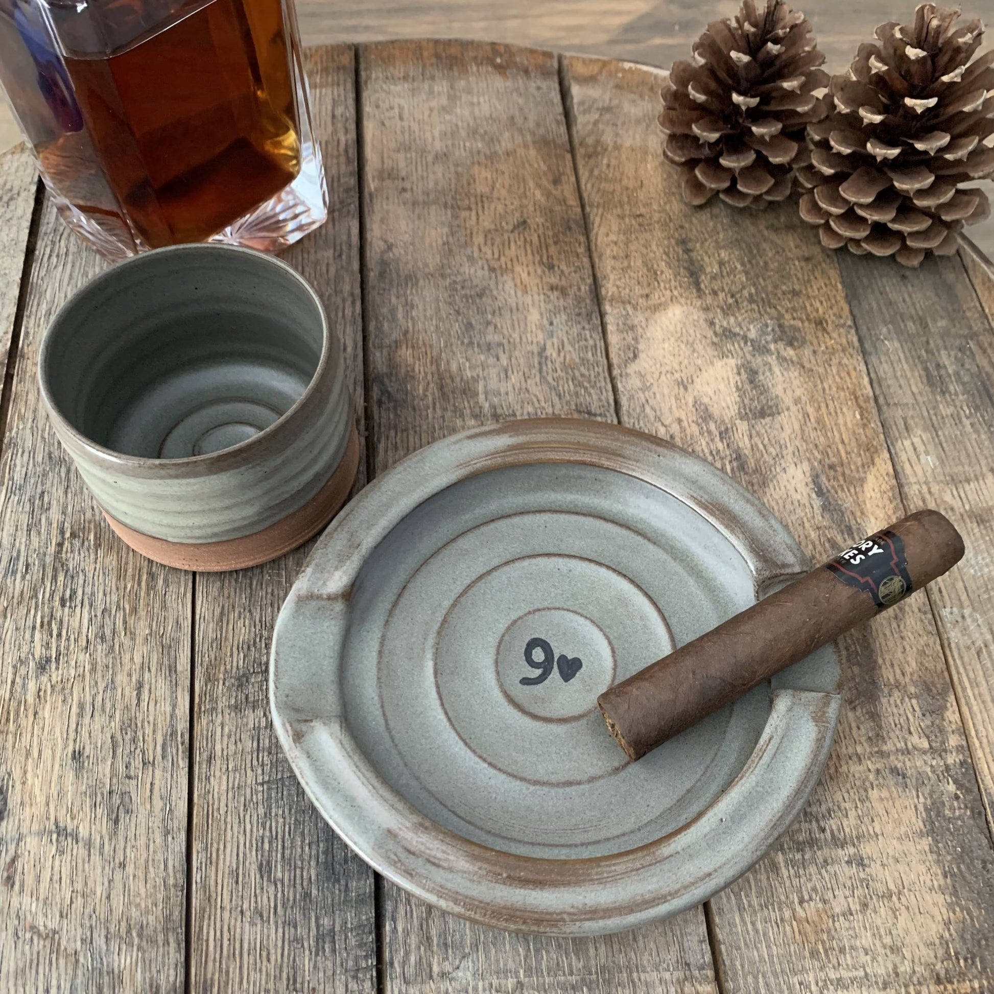 pottery set of whiskey cup and cigar tray with a 9 and heart design on a wood surface