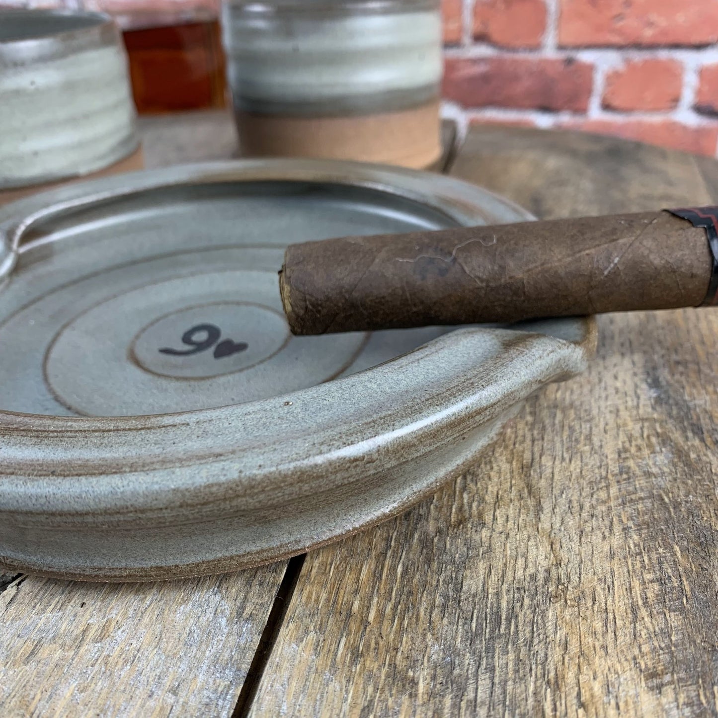 Cigar on a pottery ashtray with a brick wall in the background