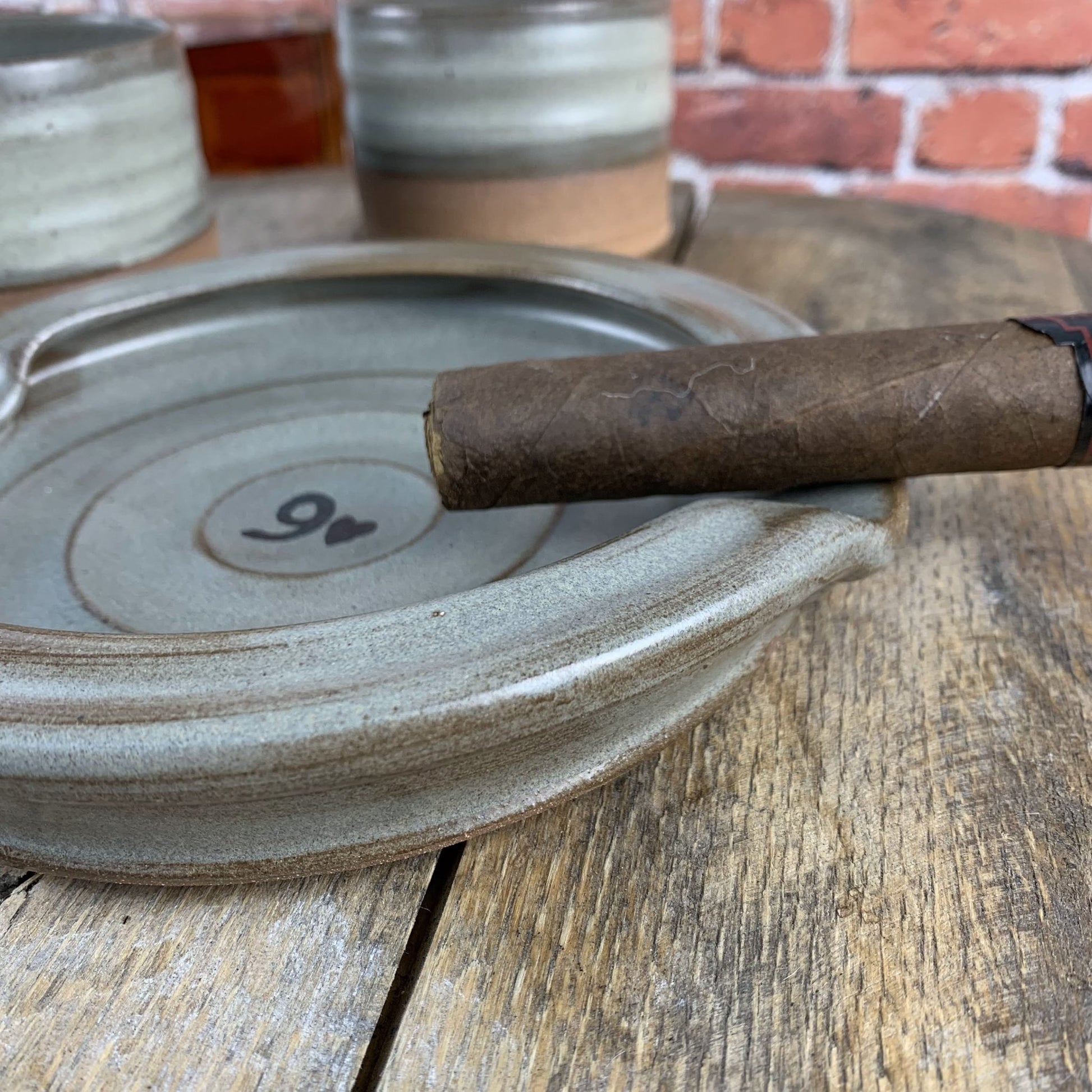Cigar on a pottery ashtray with a brick wall in the background