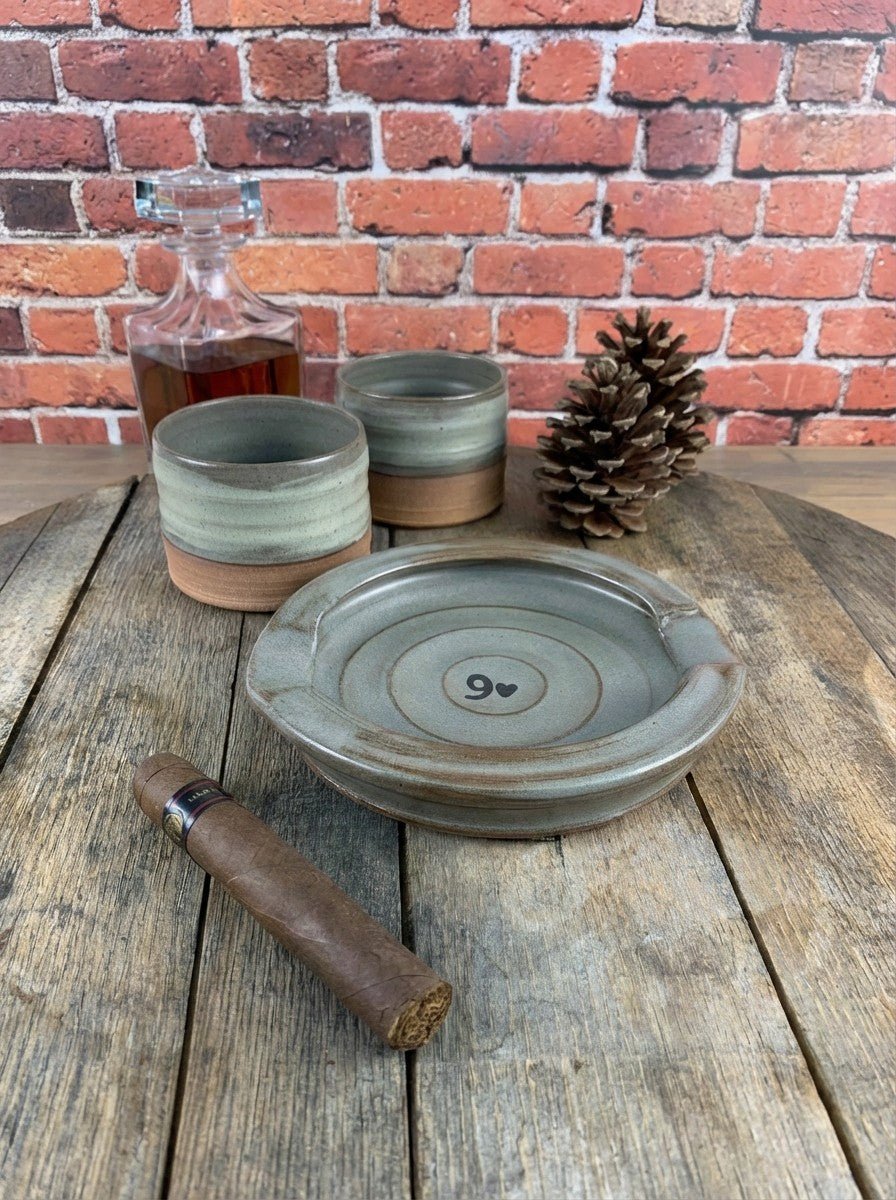 Set of ceramic tumblers and a cigar ashtray on a wooden surface with a brick wall background