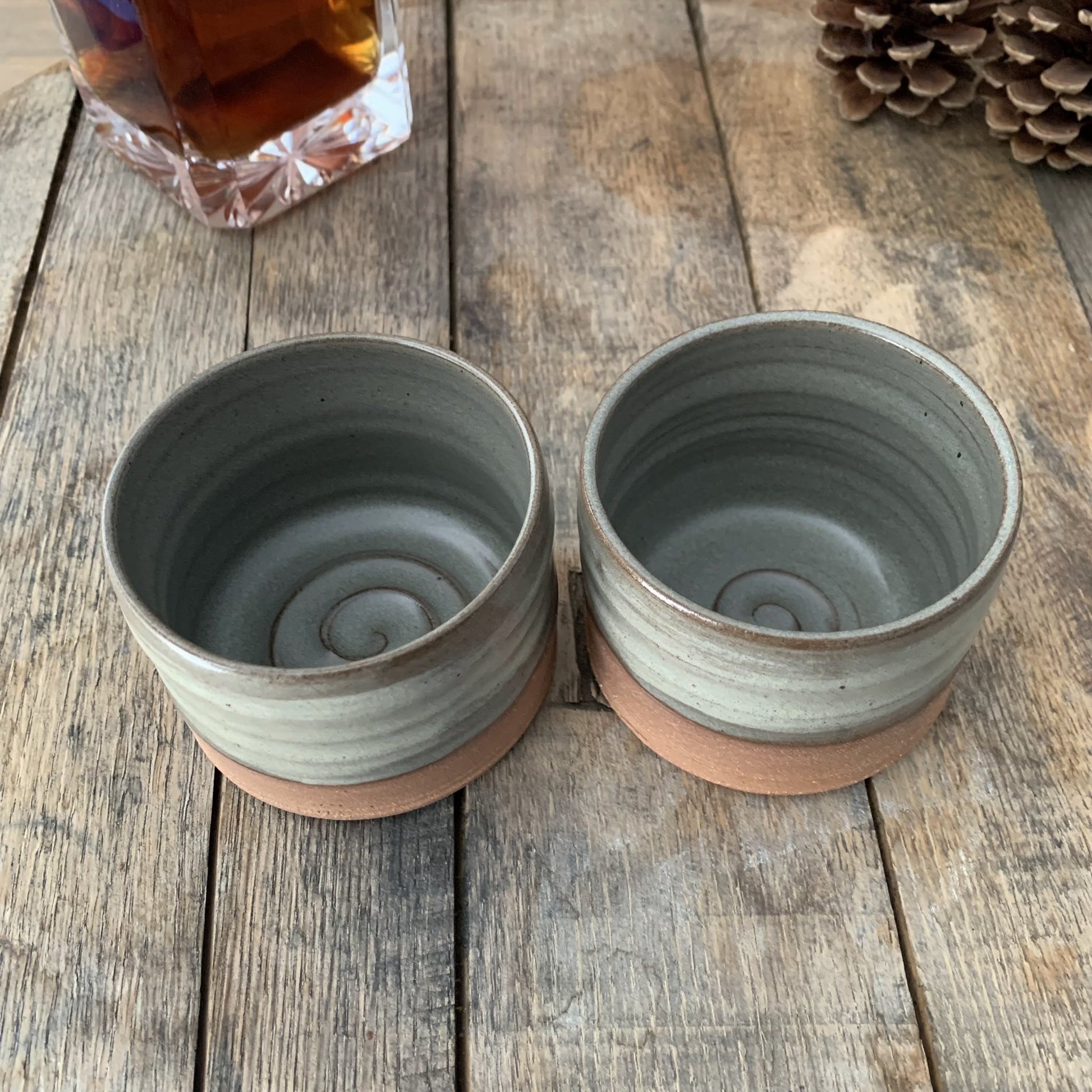 Two gray ceramic cups with brown bases on a wooden surface.