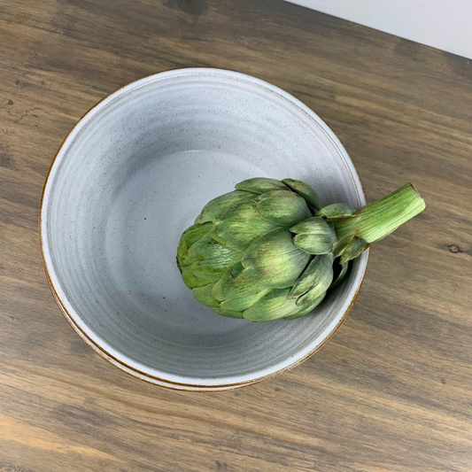 Artichoke in a white ceramic bowl on a wooden surface