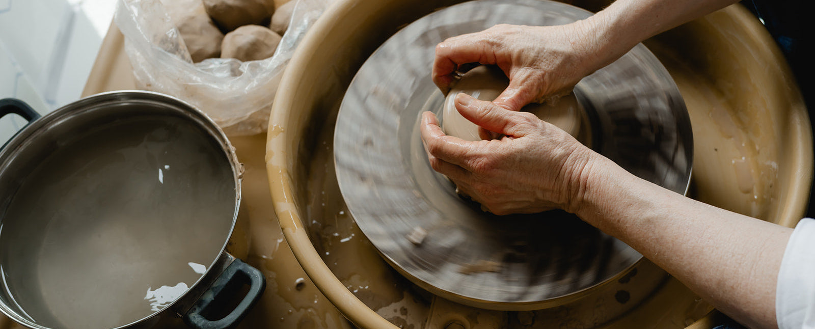 Person working with clay on a pottery wheel in a workshop setting.