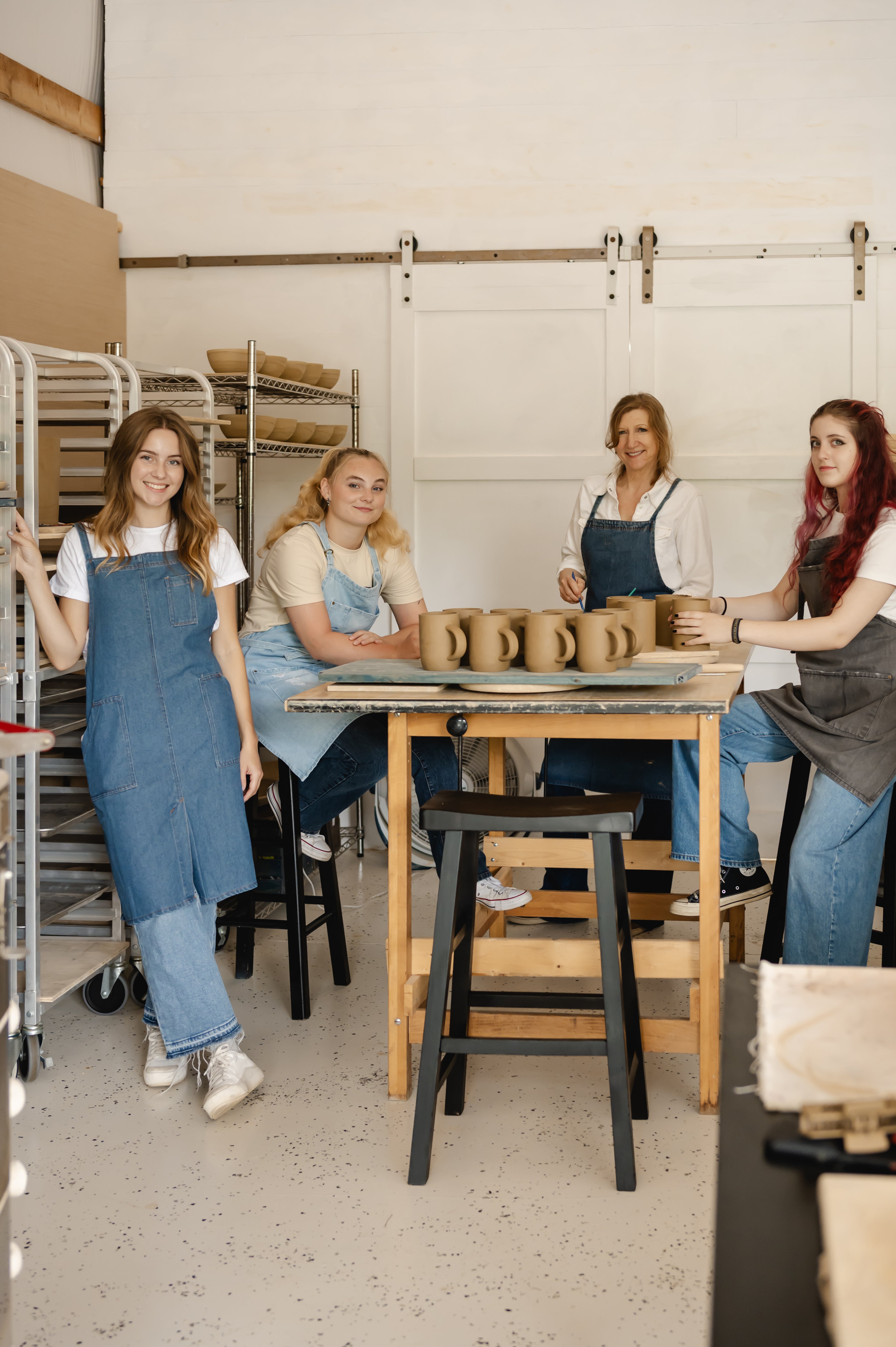 Four women in a pottery studio with clay pots on a table.