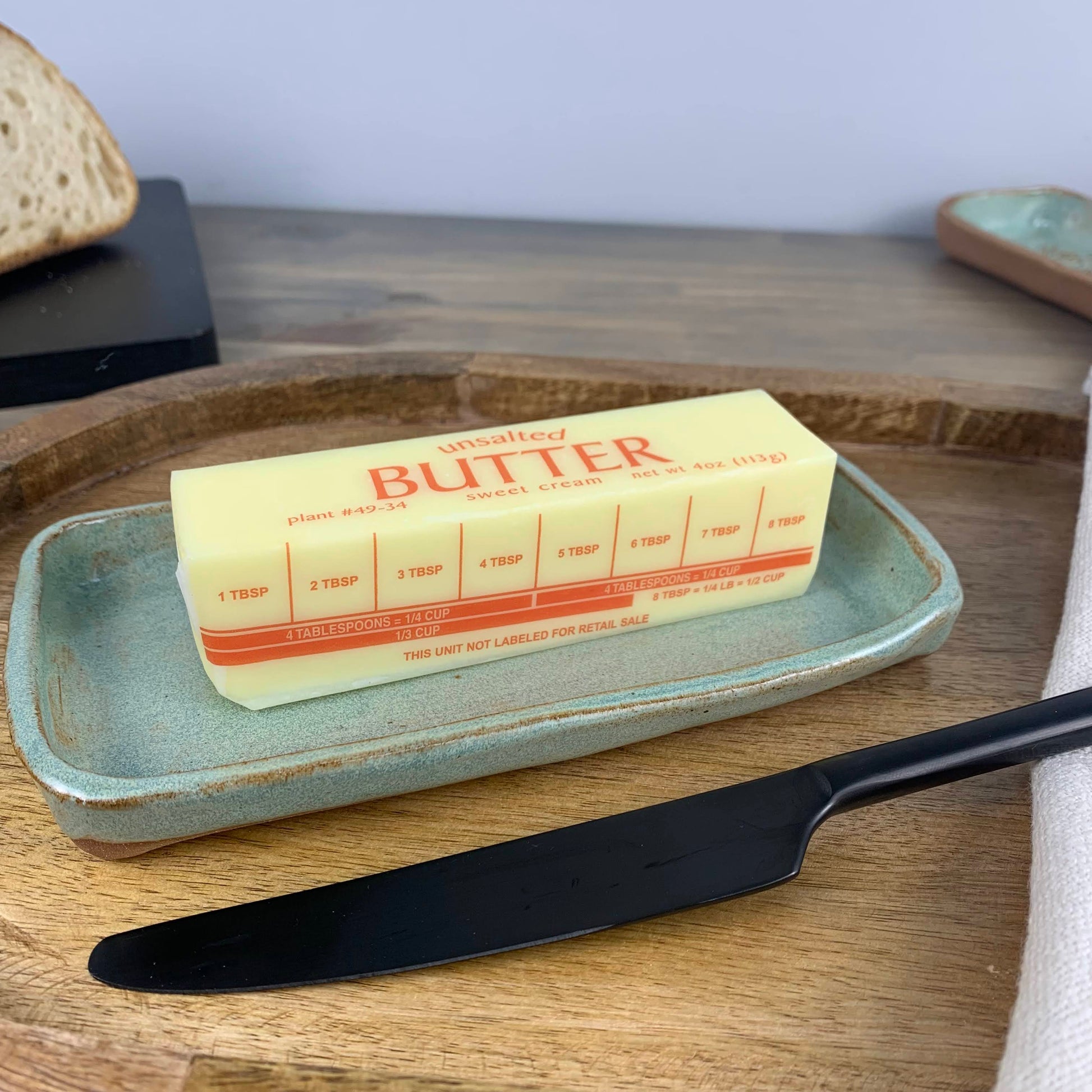 Butter stick on a ceramic tray with a knife on a wooden surface