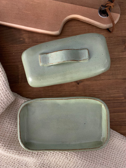 the top and bottom of a handmade pottery butter dish on wood countertop with dishcloth and cutting board