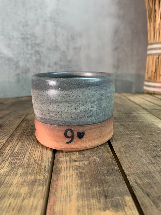 Ceramic cup with a gray glaze surface and a number 9 and heart image near the bottom sitting on wood surface