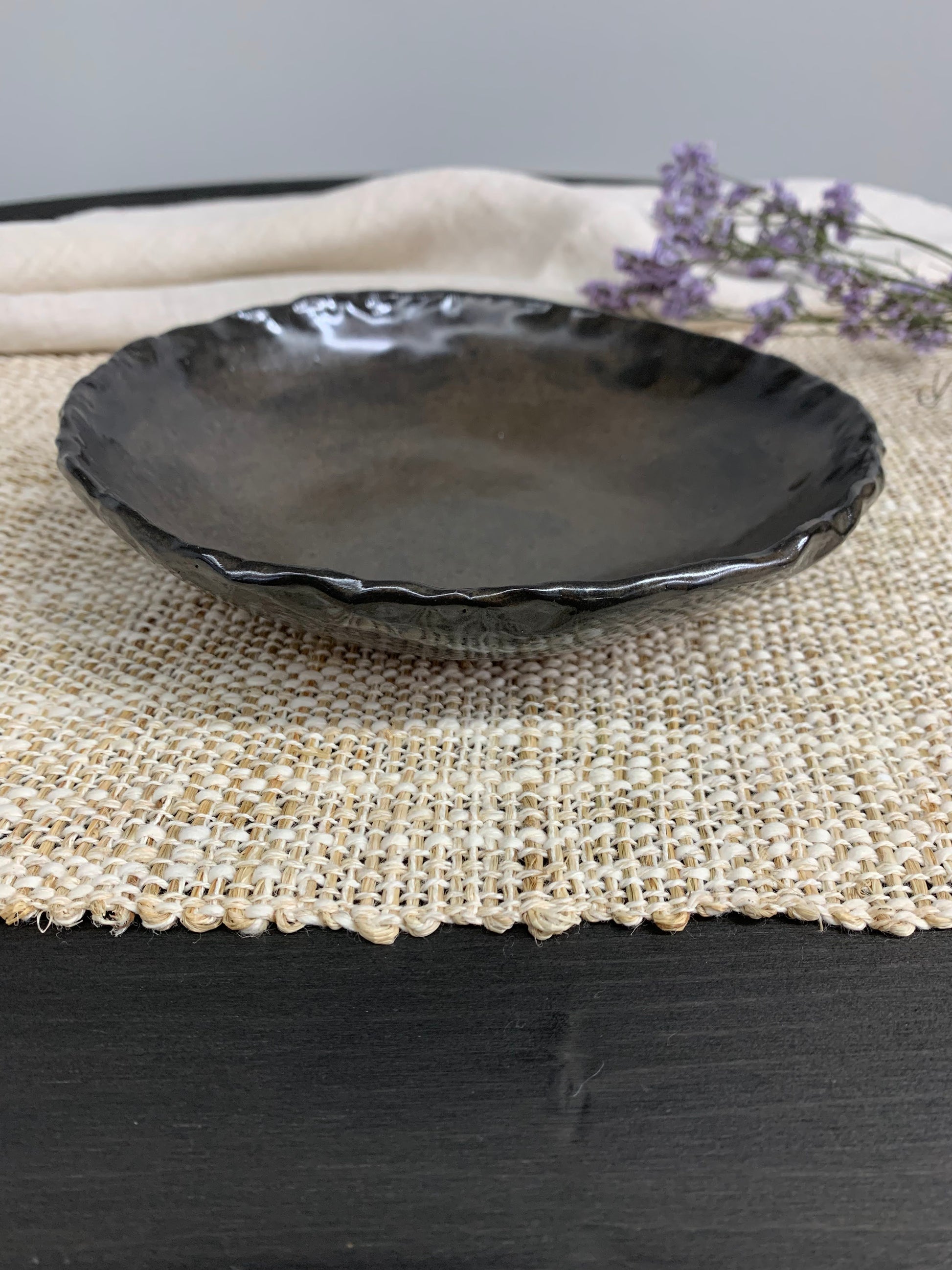 Dark handcrafted ceramic bowl and lavender flowers on a gray background